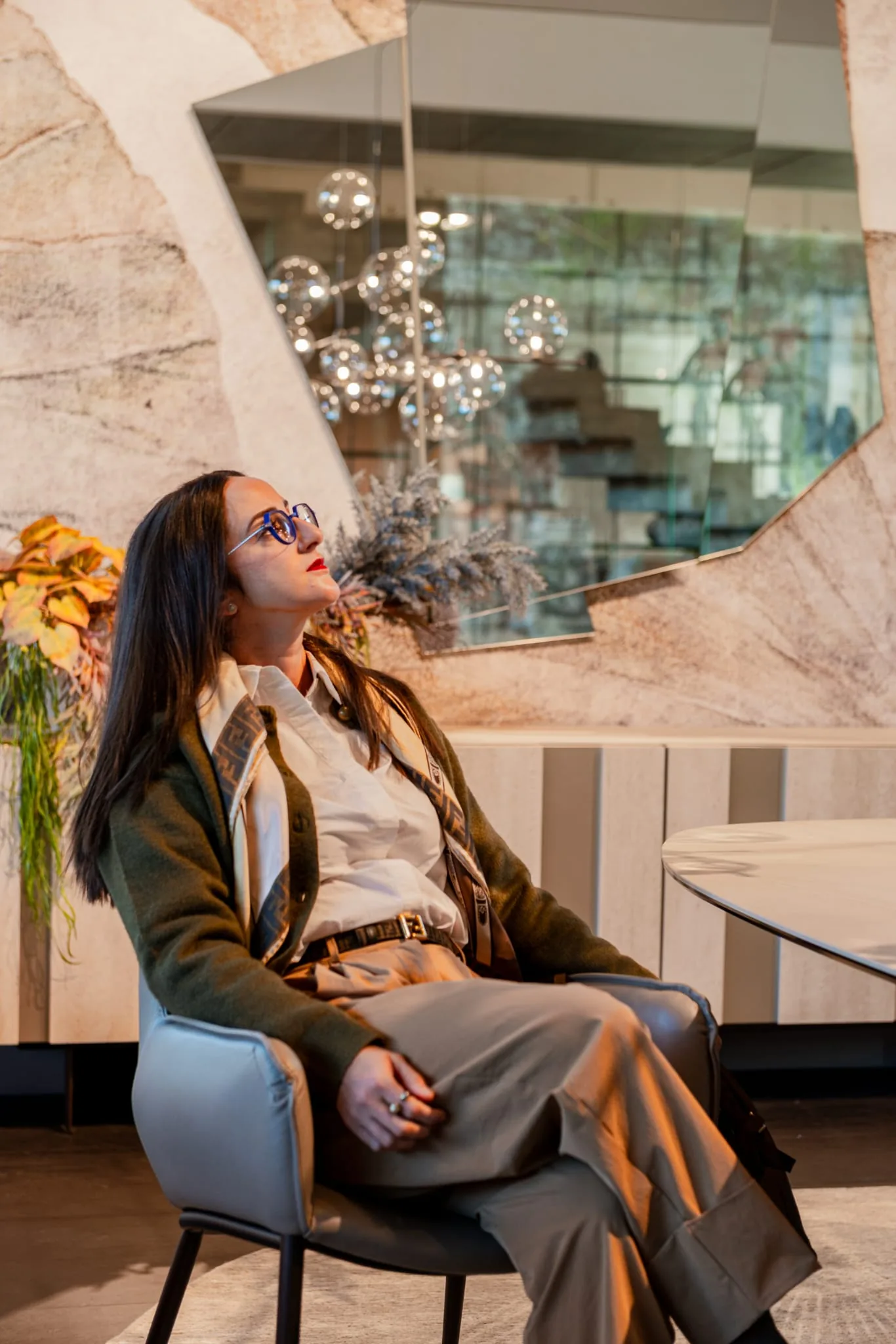 Ruba Tannous, interior designer, seated in a grey armchair beside a stone-clad wall and a large faceted mirror