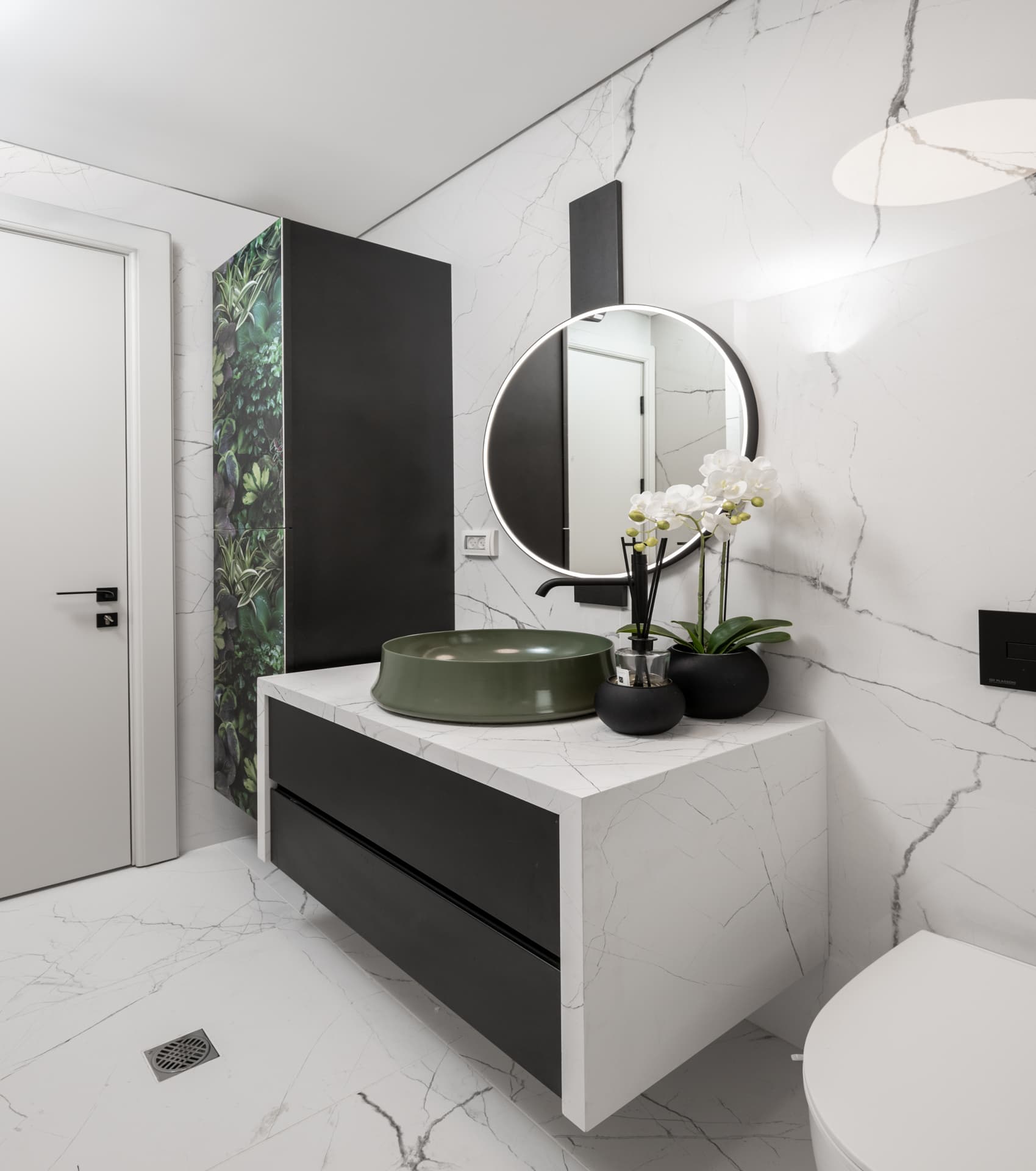 Round black-framed mirror above a green vessel basin on a white stone waterfall vanity with black drawers in a bathroom of Argamán