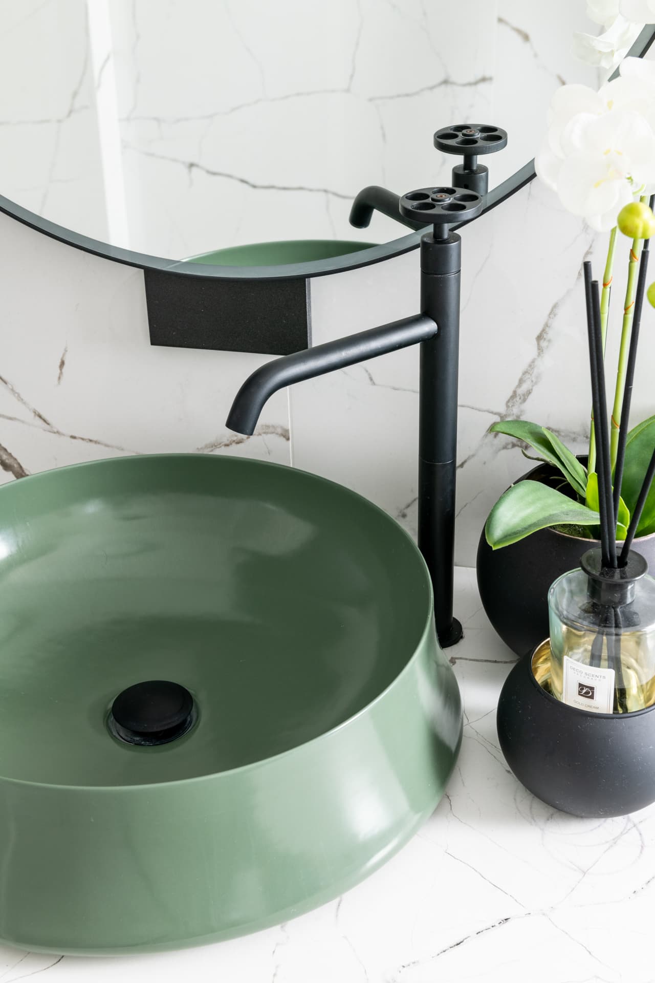 Green vessel basin with a tall matte black wheel-handle faucet on white veined stone in a bathroom of Argamán
