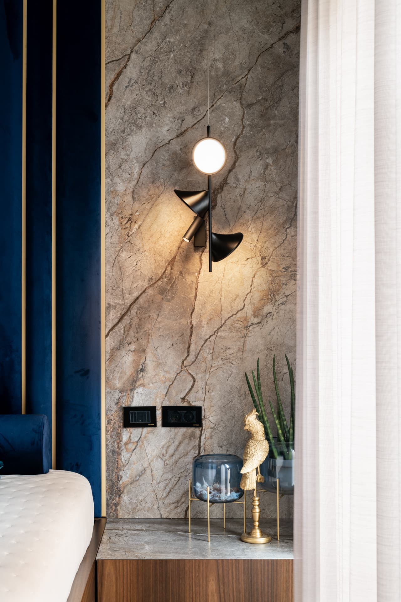 Sculptural black wall sconce on a veined stone panel beside the blue velvet headboard in the master bedroom of Argamán