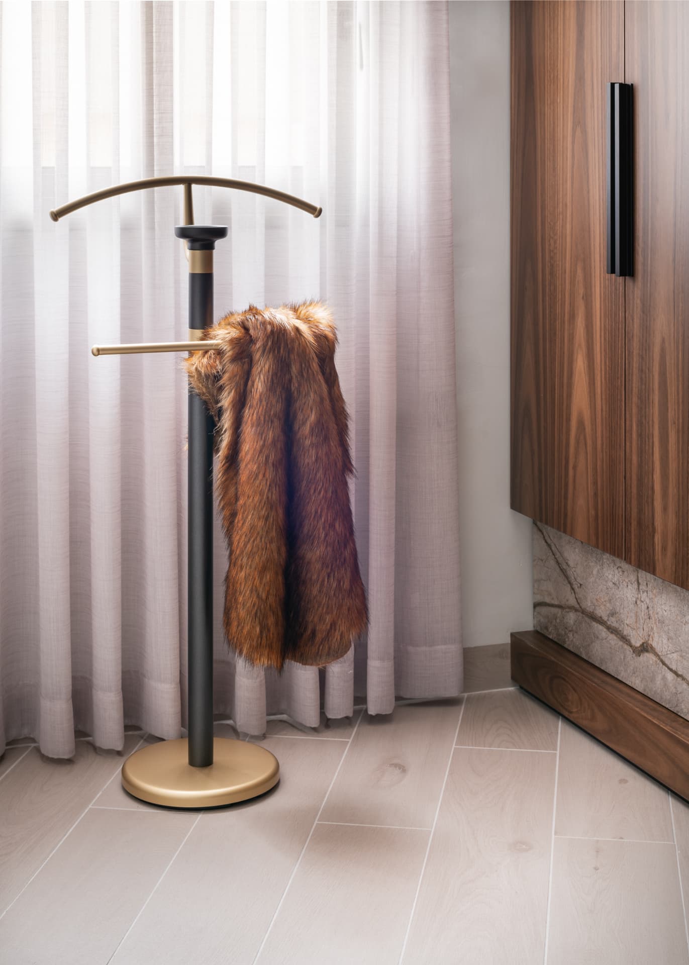 Brass and black valet stand with a fur throw beside a walnut wardrobe and sheer curtains in the master bedroom of Argamán