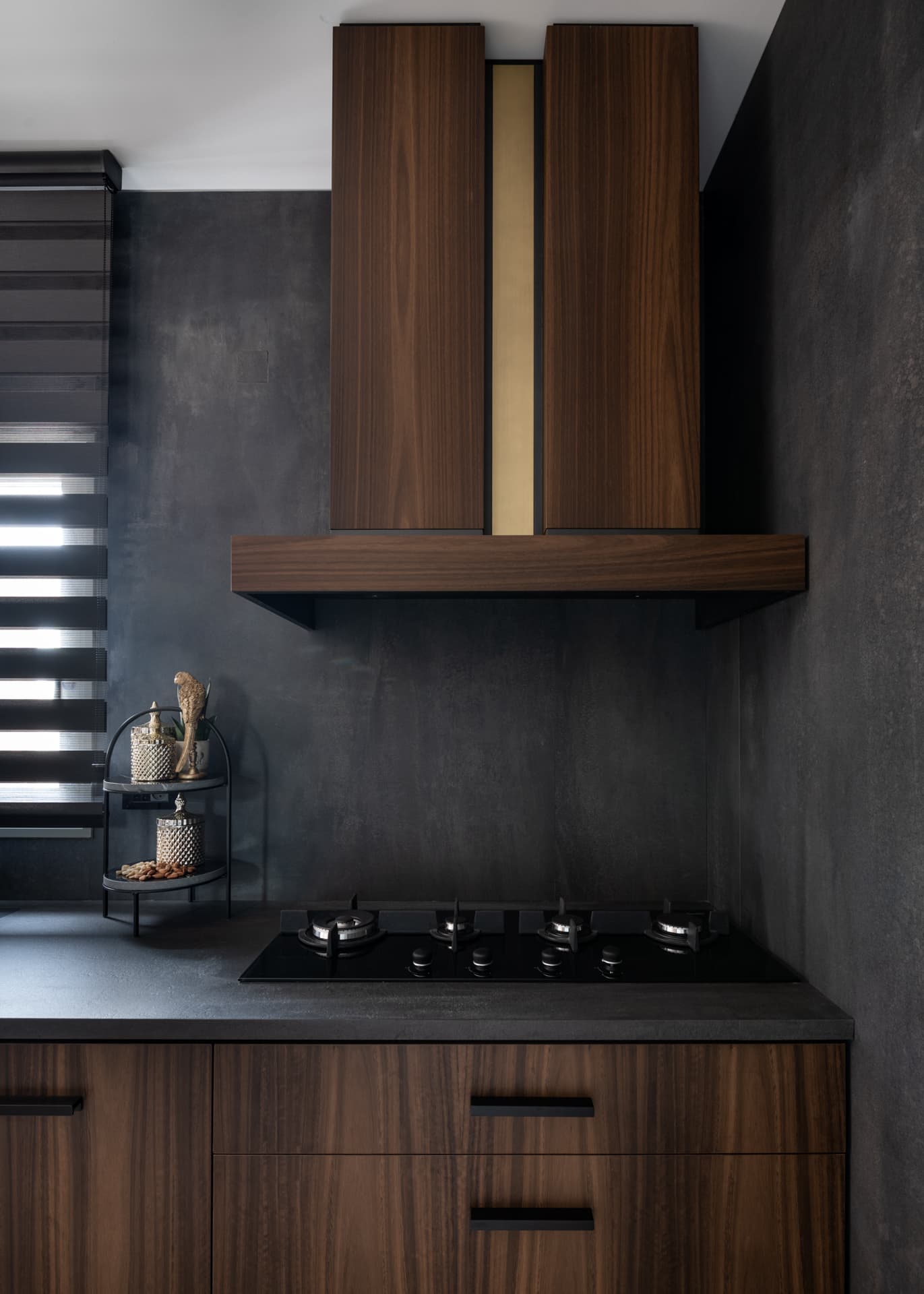 Walnut range hood with a brass inlay strip over a dark grey backsplash and gas hob in the kitchen of Argamán