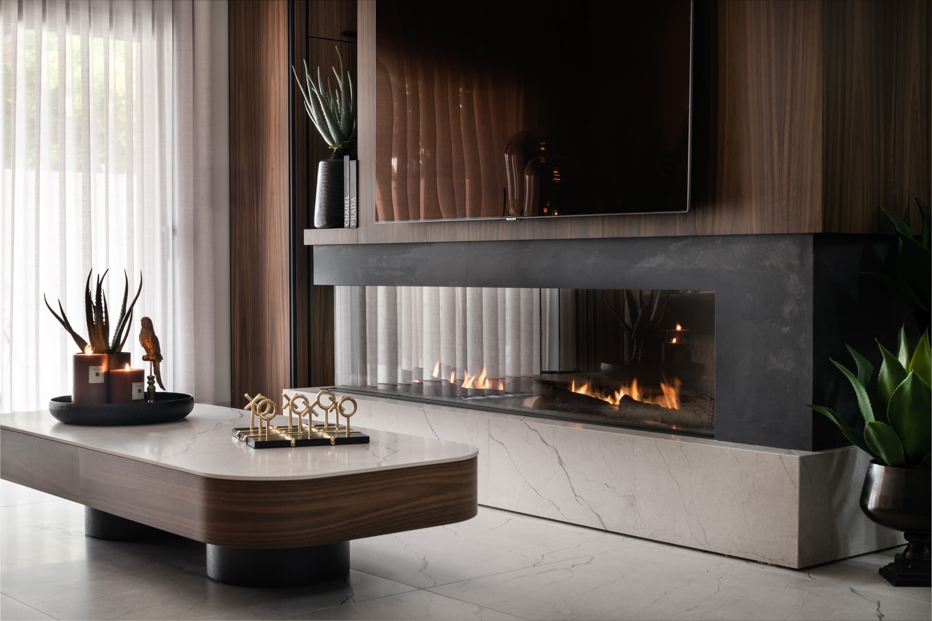 Linear glass fireplace in a veined stone base beside a rounded walnut-edged coffee table in the living room of Argamán