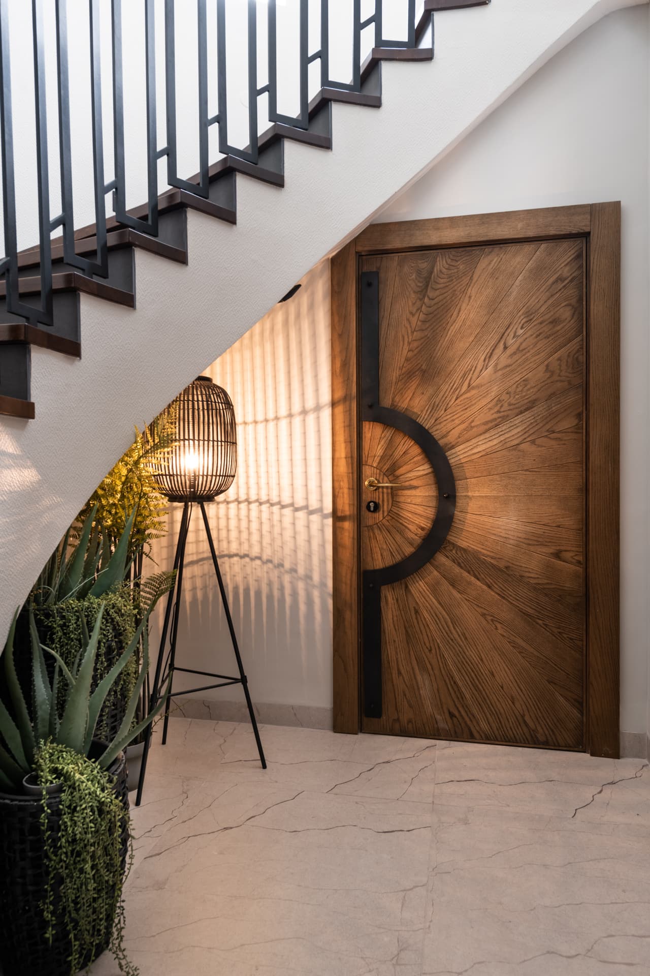 Sunburst-grain wood door with a black semicircular pull set beneath the staircase in the entrance of Argamán