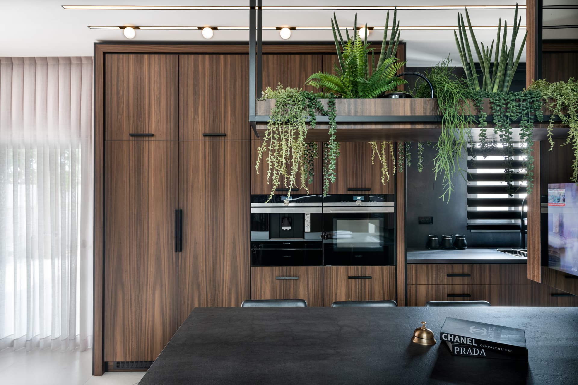 Walnut tall cabinetry with built-in ovens behind a hanging planter of trailing greenery in the kitchen of Argamán