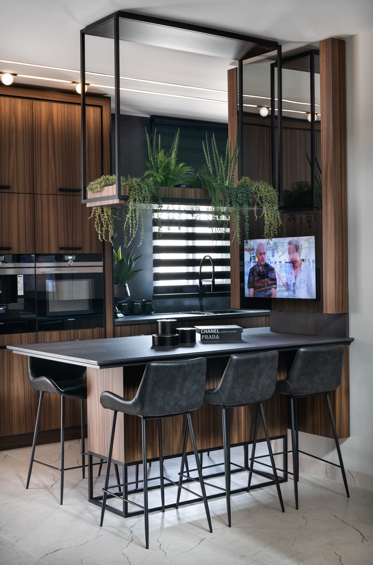 Island bar with a black steel-framed base and leather stools below a hanging planter frame in the kitchen of Argamán