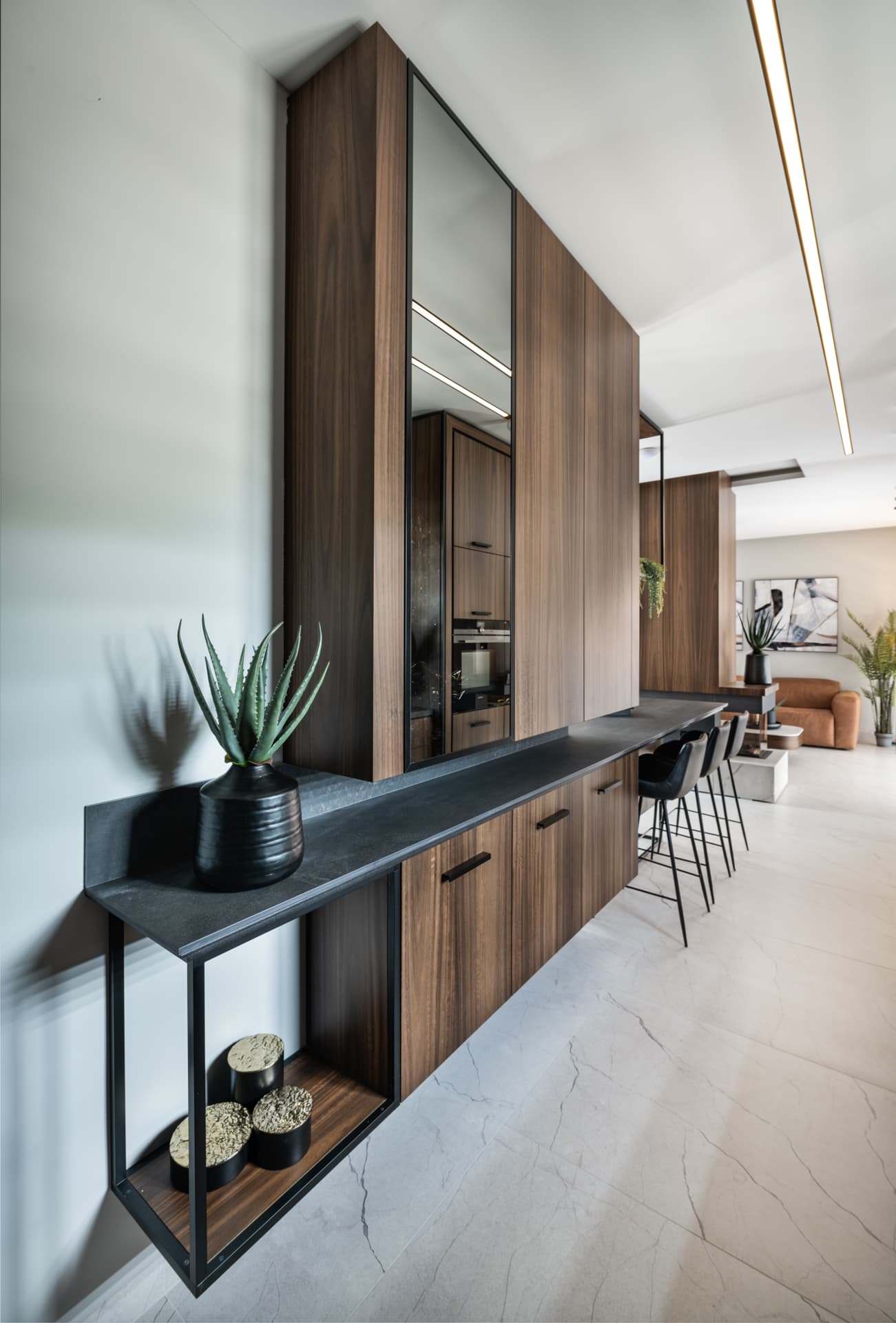 Floating dark stone ledge on a black steel frame beside a mirrored walnut tall unit in the kitchen of Argamán