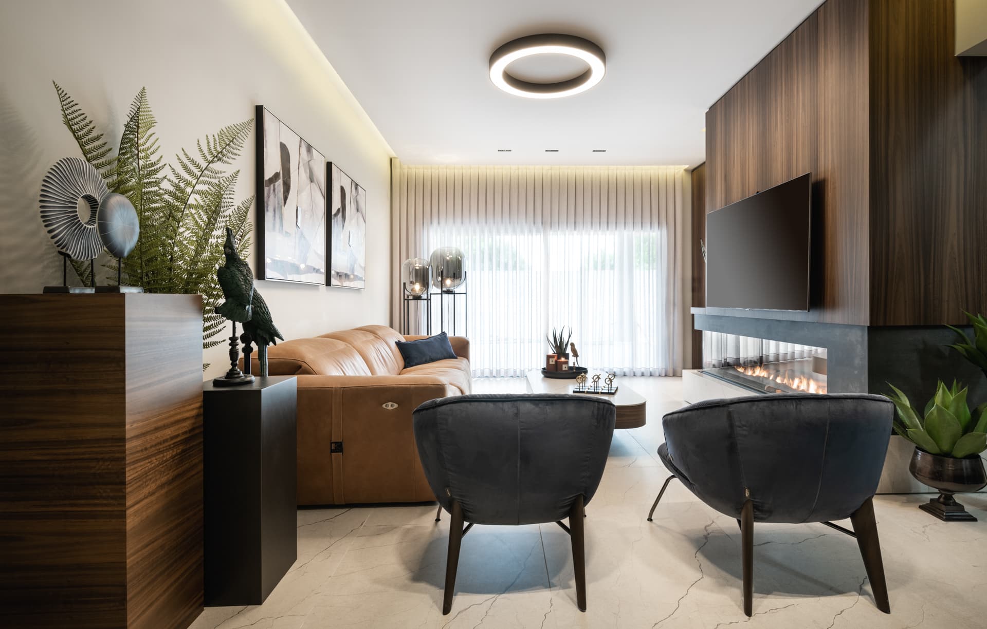 Living room with cove lighting on, a ring ceiling light and a lit linear fireplace beneath the walnut media wall in Argamán