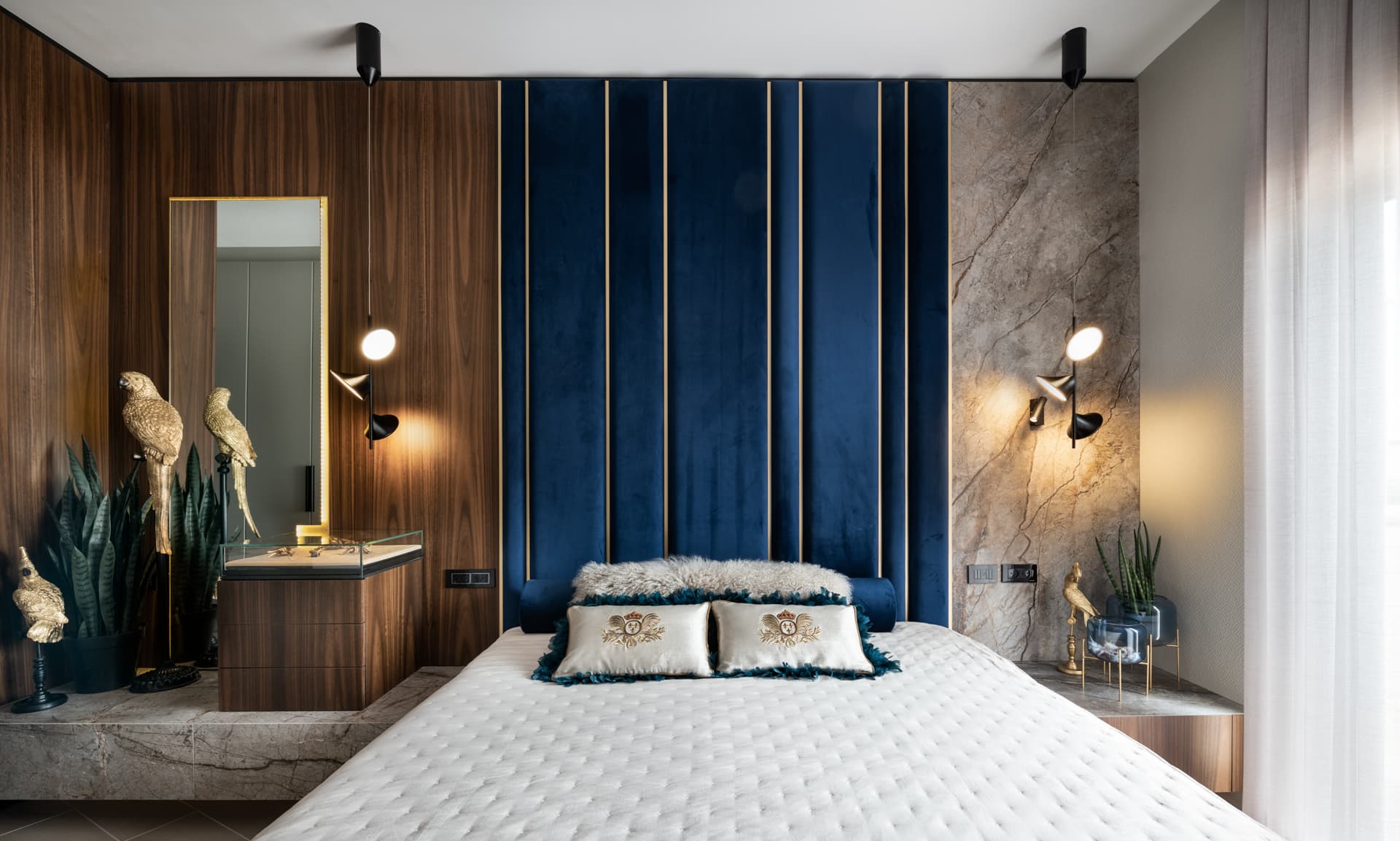 Full-height blue velvet channel headboard wall with brass inlays between walnut panels and veined stone in the master bedroom of Argamán