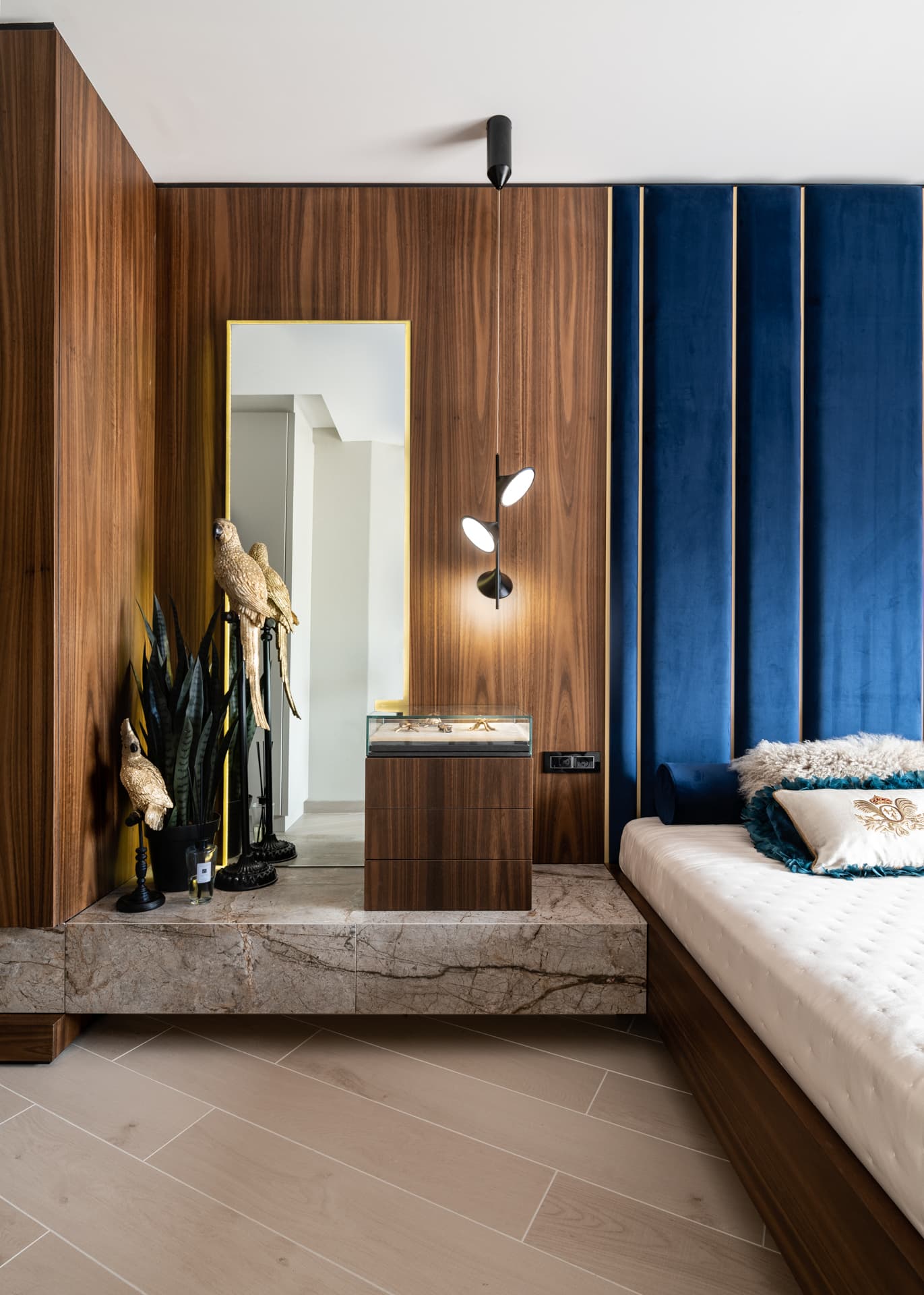 Vanity nook with a brass-framed mirror, black pendant sconce and brass parrot figurines on a stone plinth in the master bedroom of Argamán