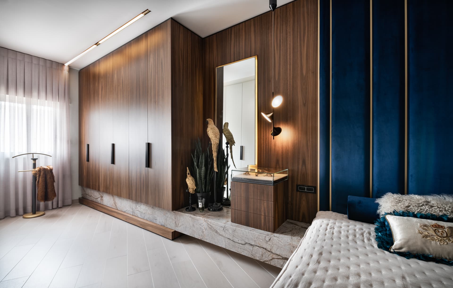 Walnut wardrobe run on a veined stone plinth leading to a mirrored vanity nook in the master bedroom of Argamán