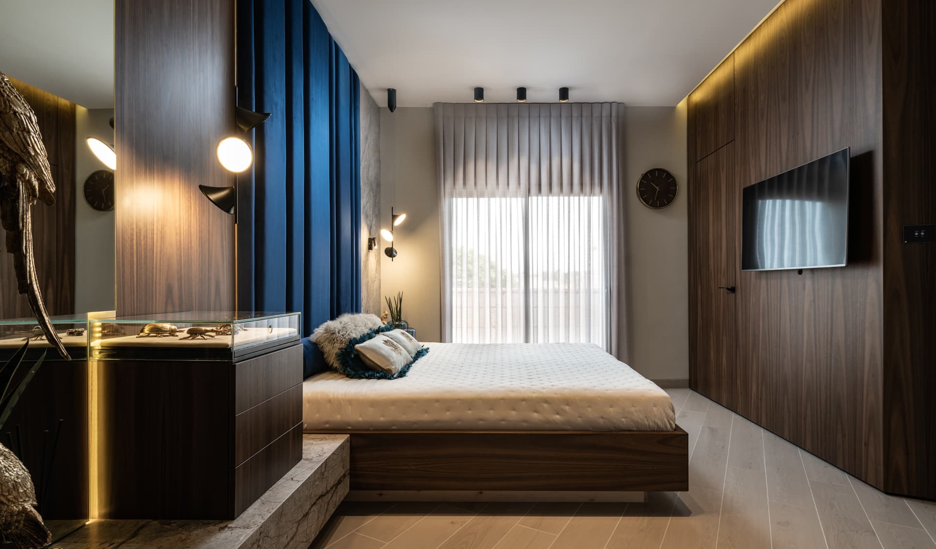 Master bedroom with lit wall sconces, backlit walnut panels and a floating bed before sheer curtains in Argamán