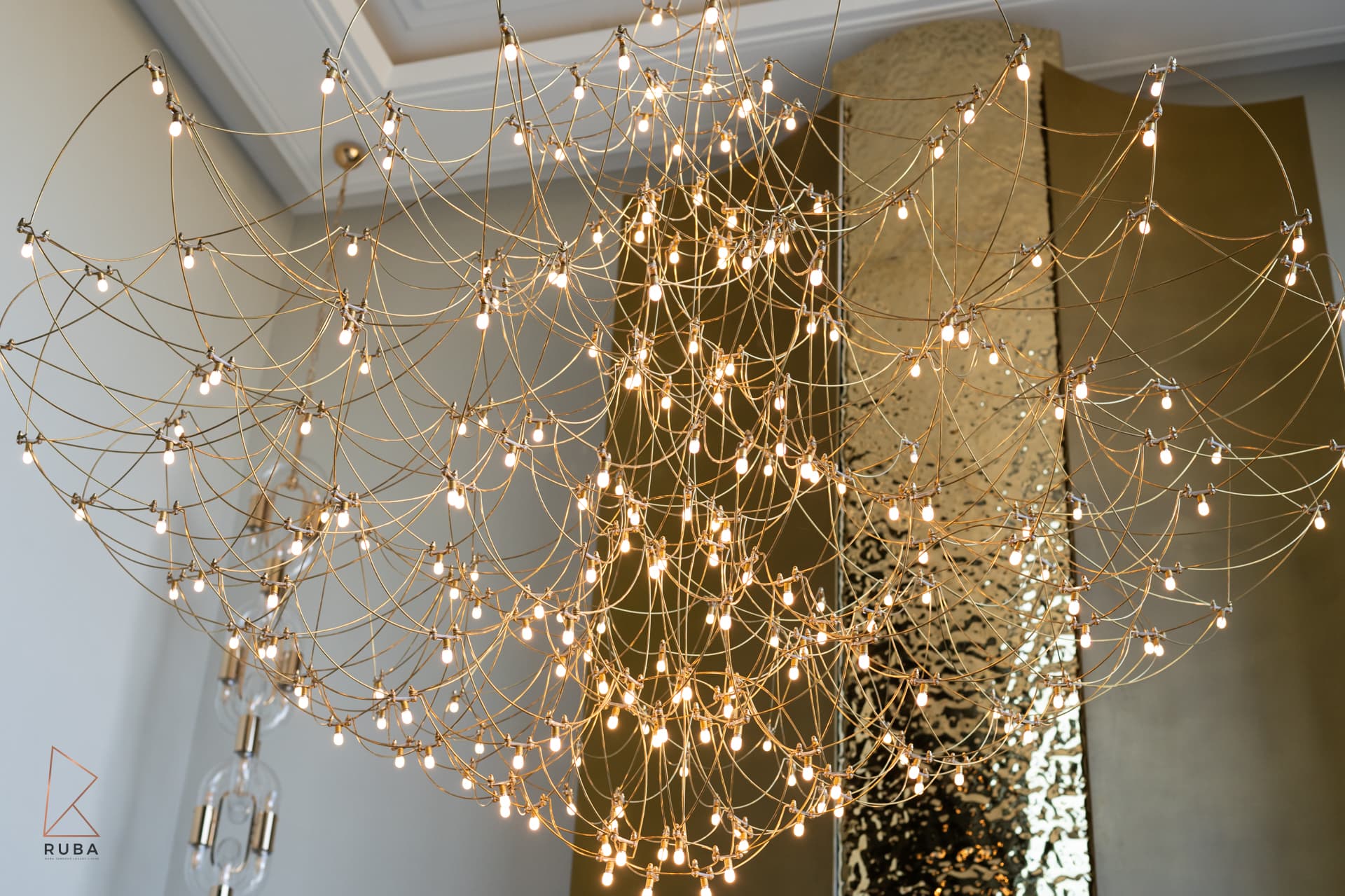 Gold wire chandelier with tiny bulbs in front of the hammered brass fireplace hood in the living room of Bird of Paradise Flower