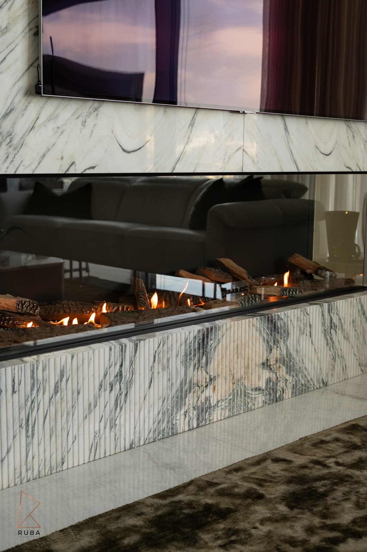 Fluted marble base of the linear gas fireplace with glowing logs in the living room of Bird of Paradise Flower
