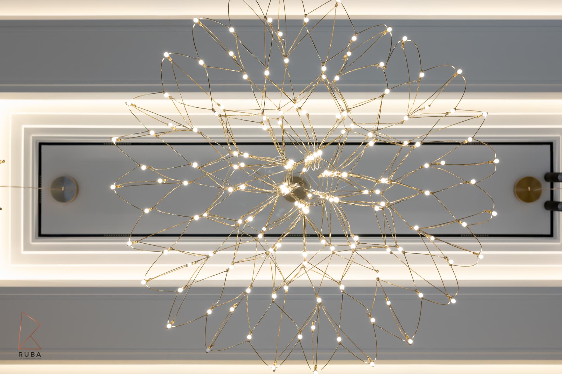 Wire starburst chandelier seen from directly below against a backlit ceiling panel in the stairwell of Bird of Paradise Flower