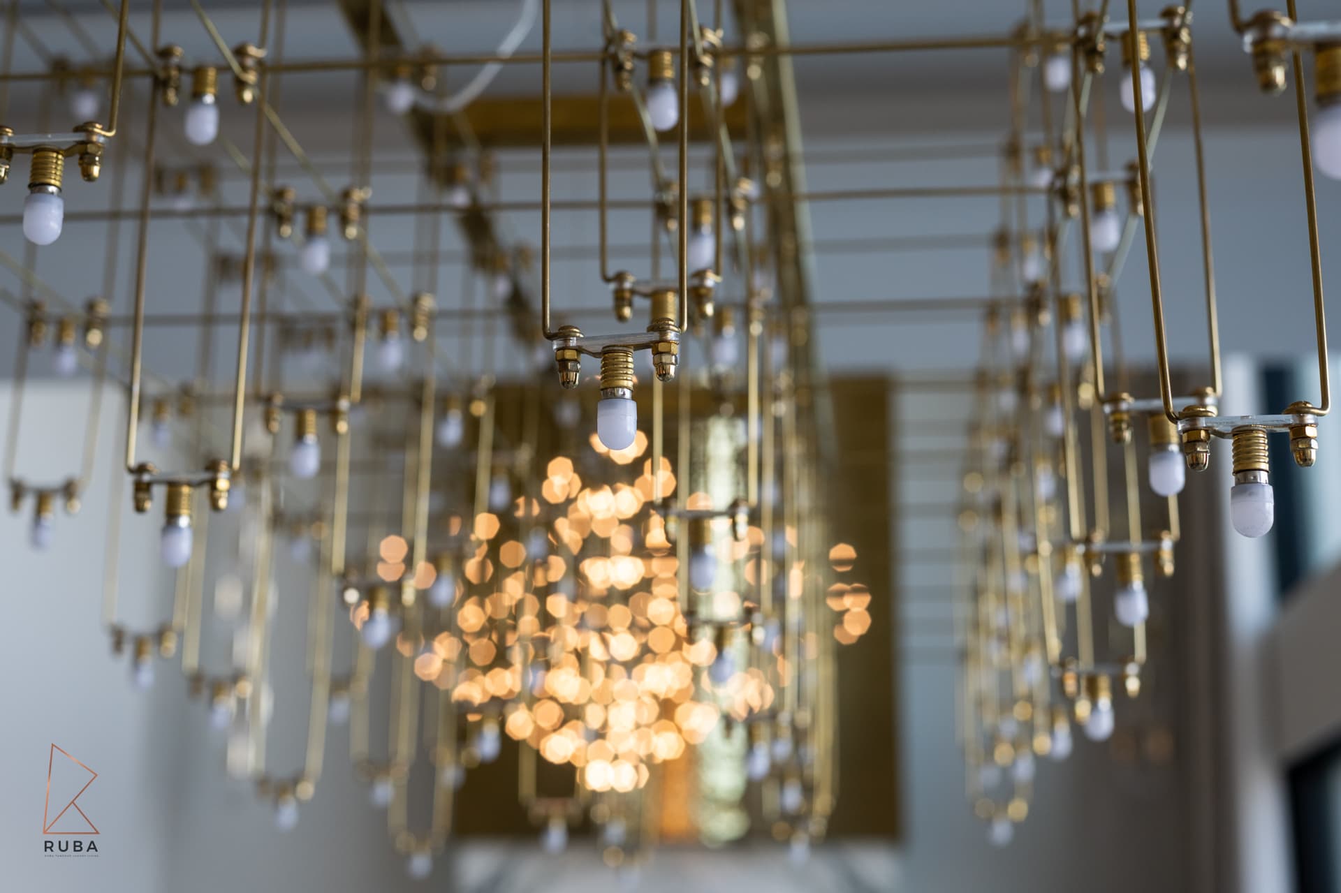 Brass grid chandelier with hanging frosted bulbs, a warm glow behind, in the dining room of Bird of Paradise Flower