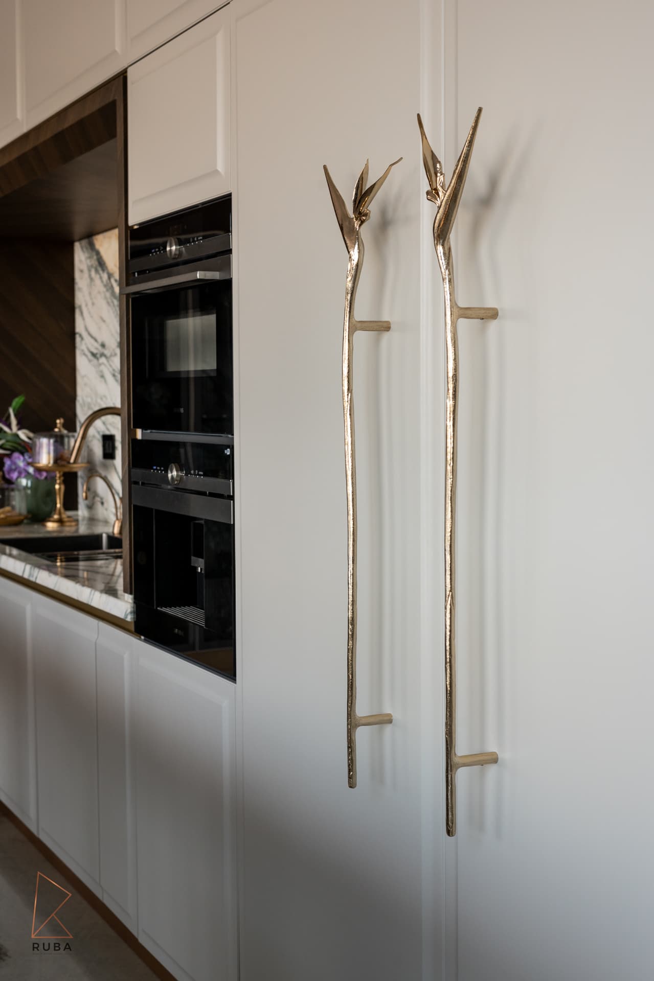 Pair of brass bird-of-paradise door pulls on white tall cabinets next to the ovens in the kitchen of Bird of Paradise Flower