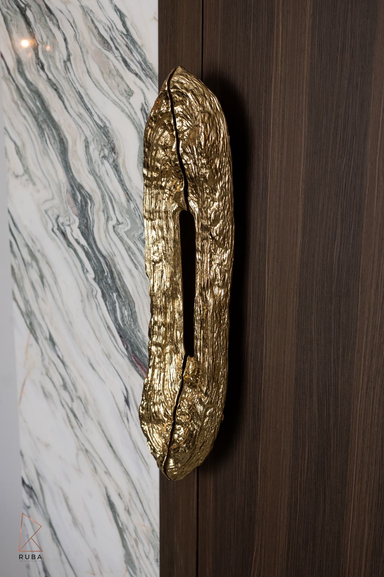Sculpted brass door pull on a dark wood door beside a veined marble strip in the master bedroom of Bird of Paradise Flower