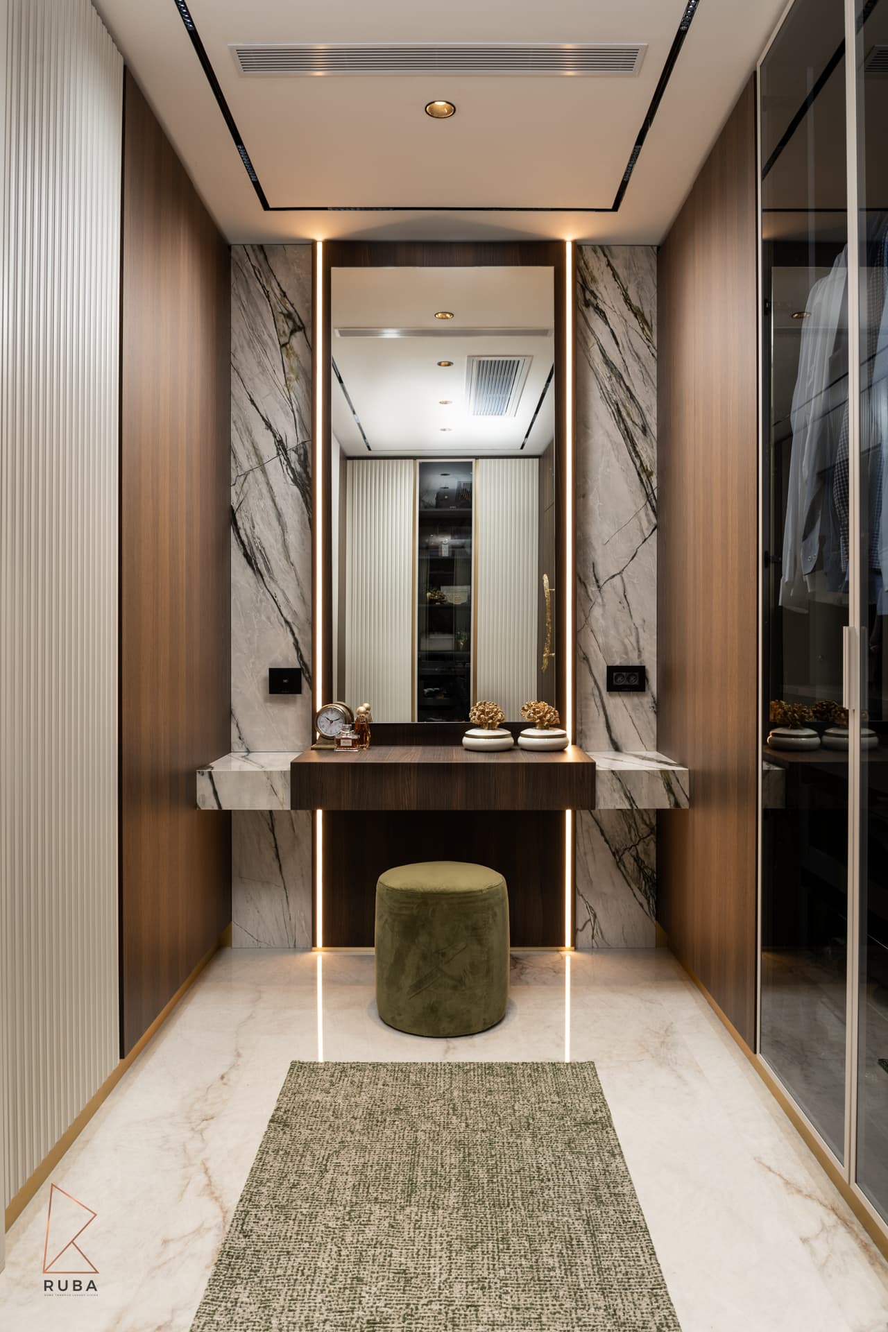 Dressing room with a backlit mirrored vanity in veined stone, a sage velvet pouf and glass wardrobes in Bird of Paradise Flower