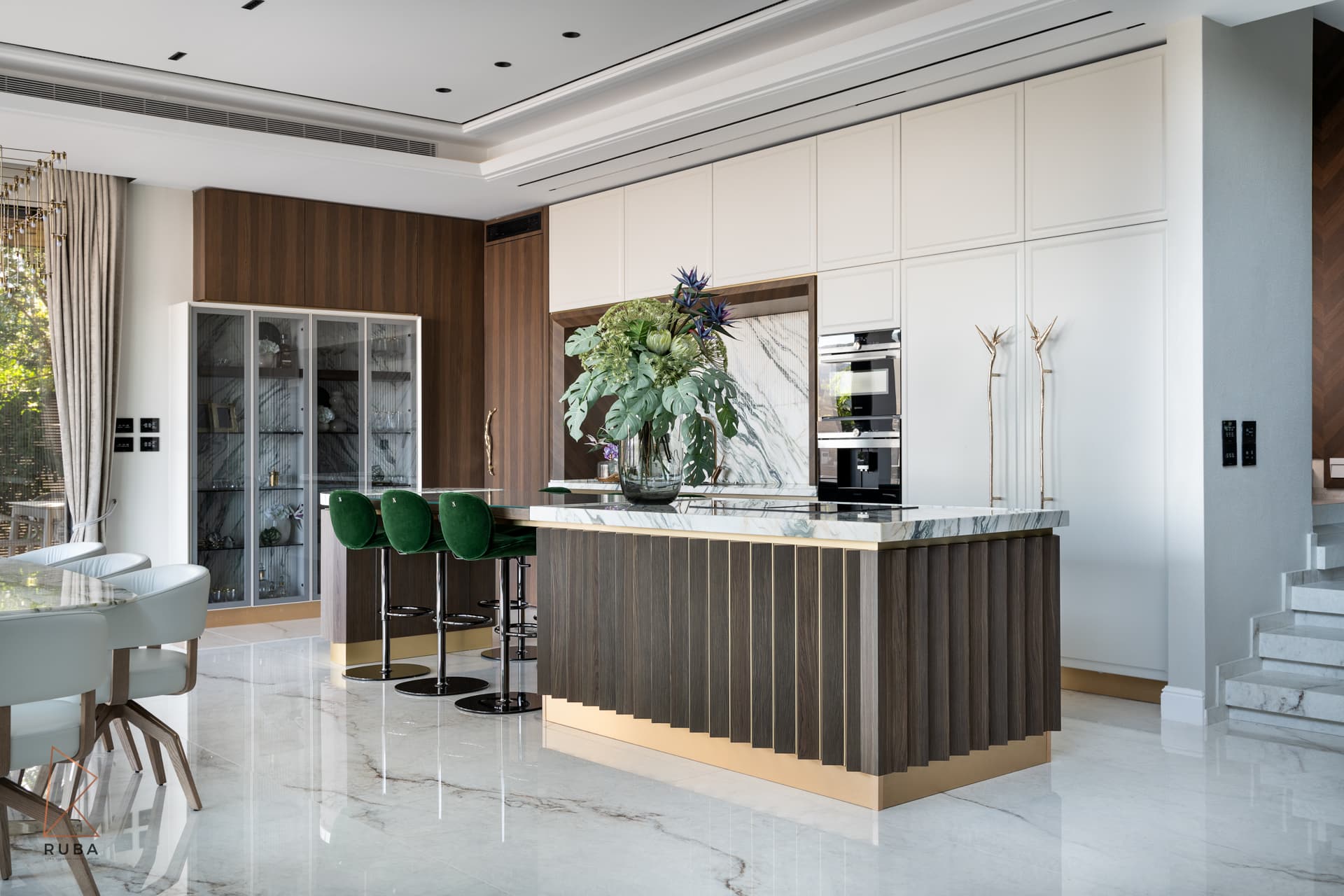 Kitchen with a fluted dark wood island, green velvet bar stools and white panelled tall cabinets in Bird of Paradise Flower