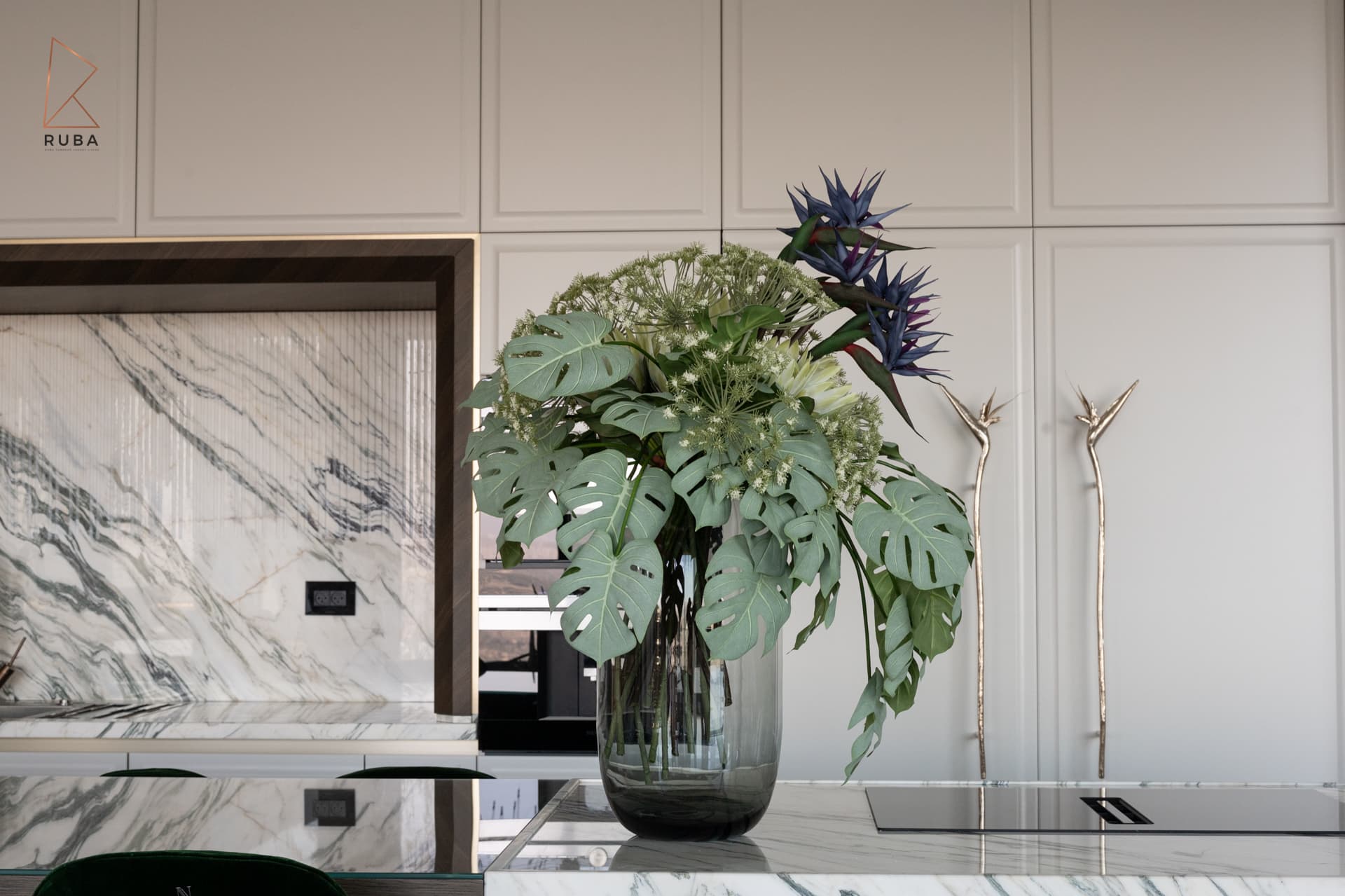 Tropical floral arrangement on the marble island before bird-shaped brass pulls on white cabinets in the kitchen of Bird of Paradise Flower