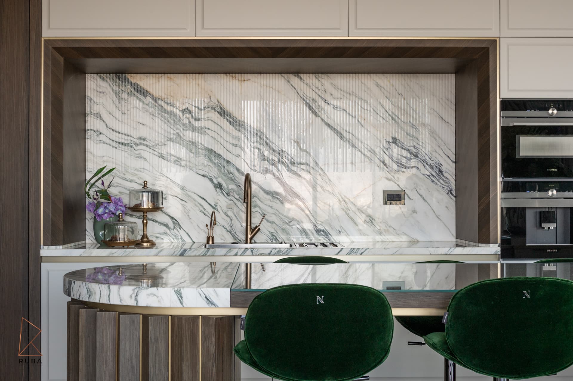 Fluted green-veined marble backsplash in a wood-framed niche with a bronze faucet in the kitchen of Bird of Paradise Flower