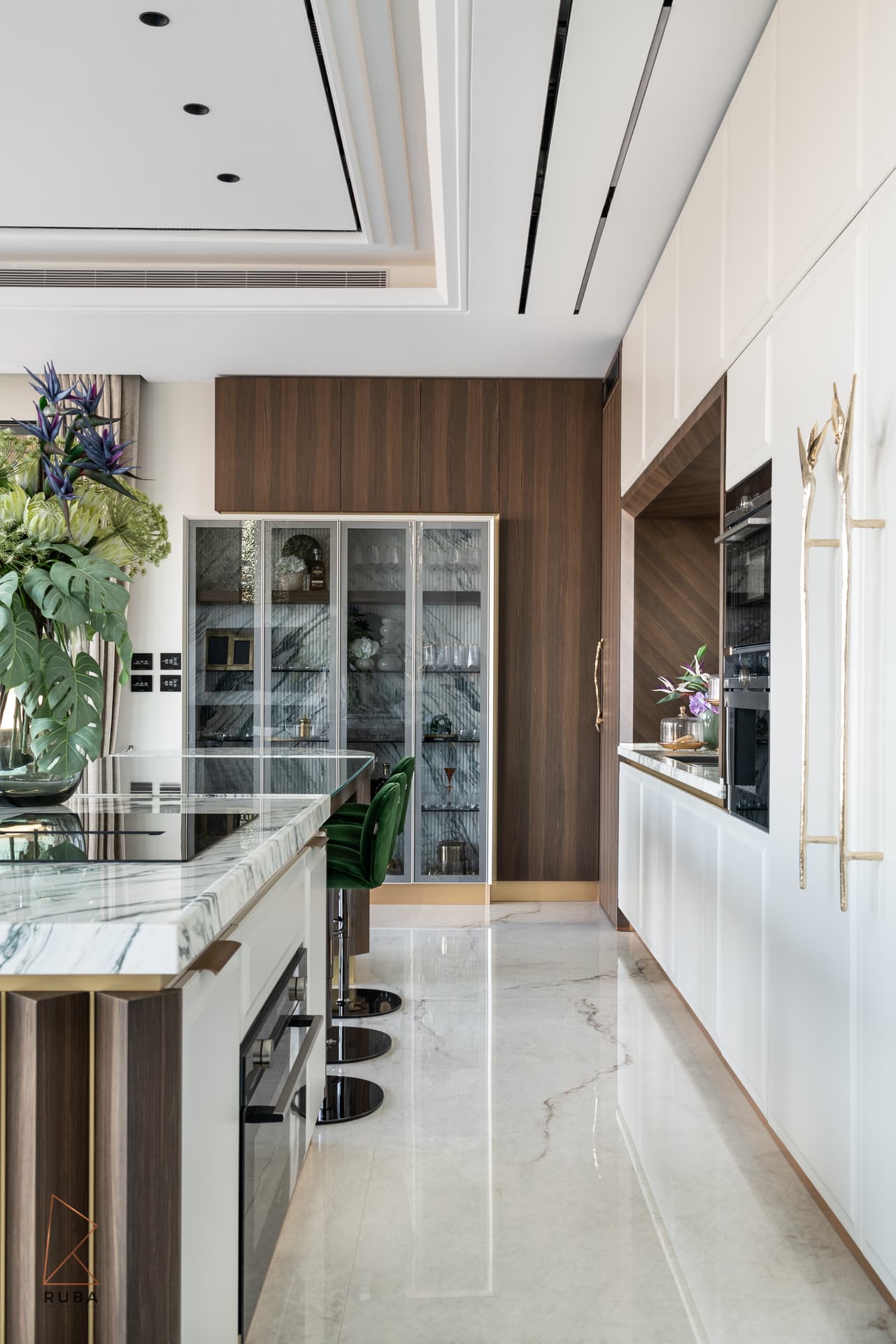 Galley view along the marble island toward a glass display cabinet and dark wood wall in the kitchen of Bird of Paradise Flower