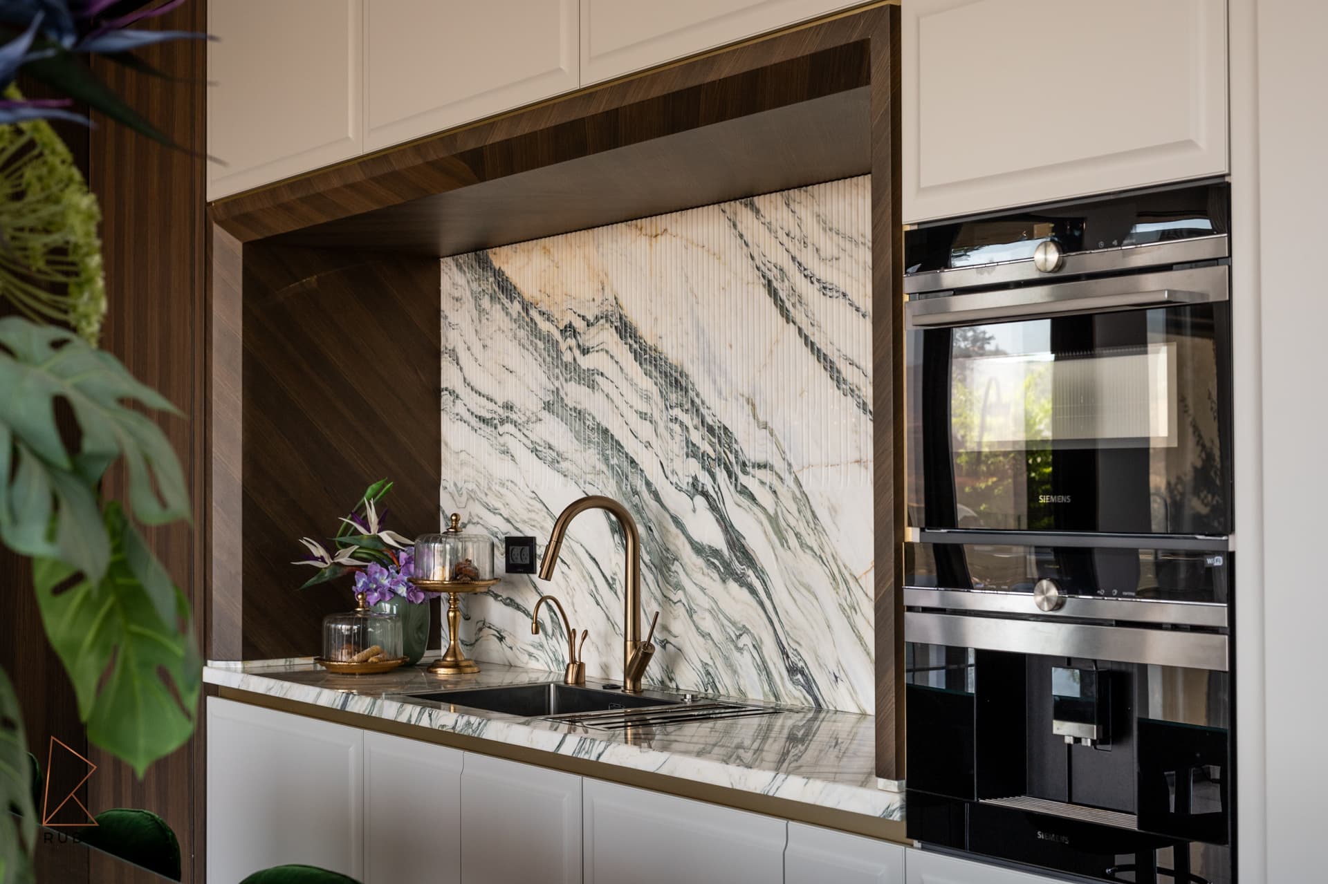 Side view of the veined marble backsplash niche beside built-in ovens and white panelled cabinets in the kitchen of Bird of Paradise Flower