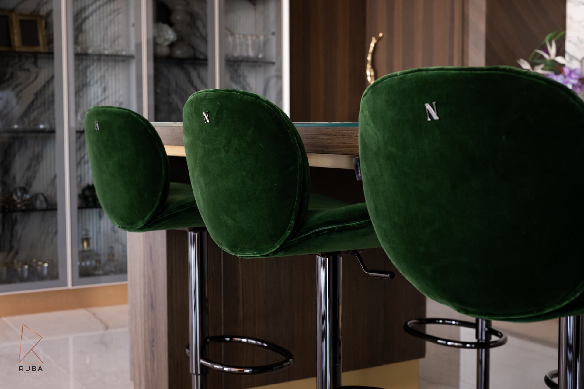 Close view of curved green velvet bar stool backs on dark chrome bases at the island in the kitchen of Bird of Paradise Flower