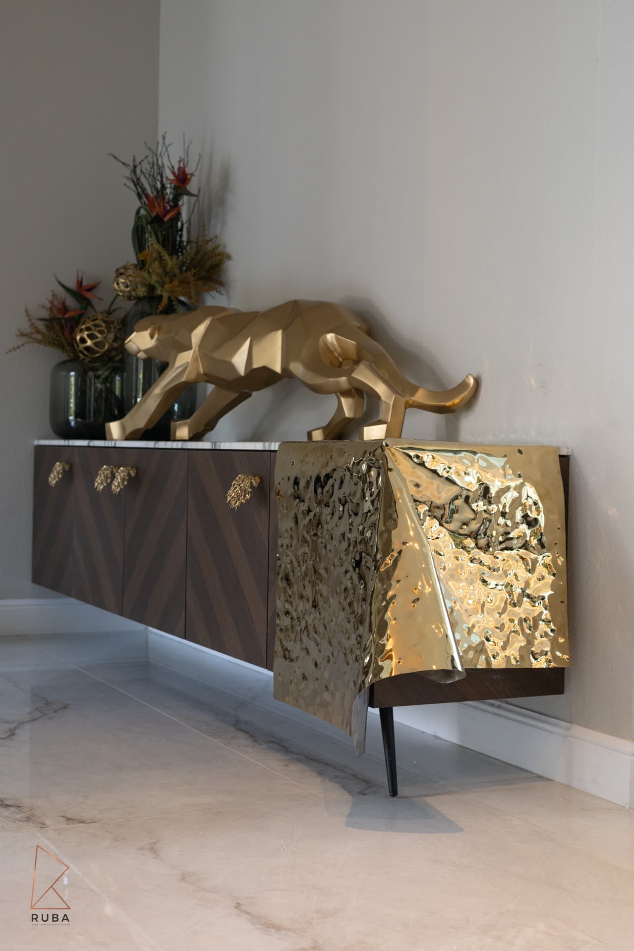 Faceted gold panther sculpture on a chevron wood sideboard with a draped brass end in the living room of Bird of Paradise Flower