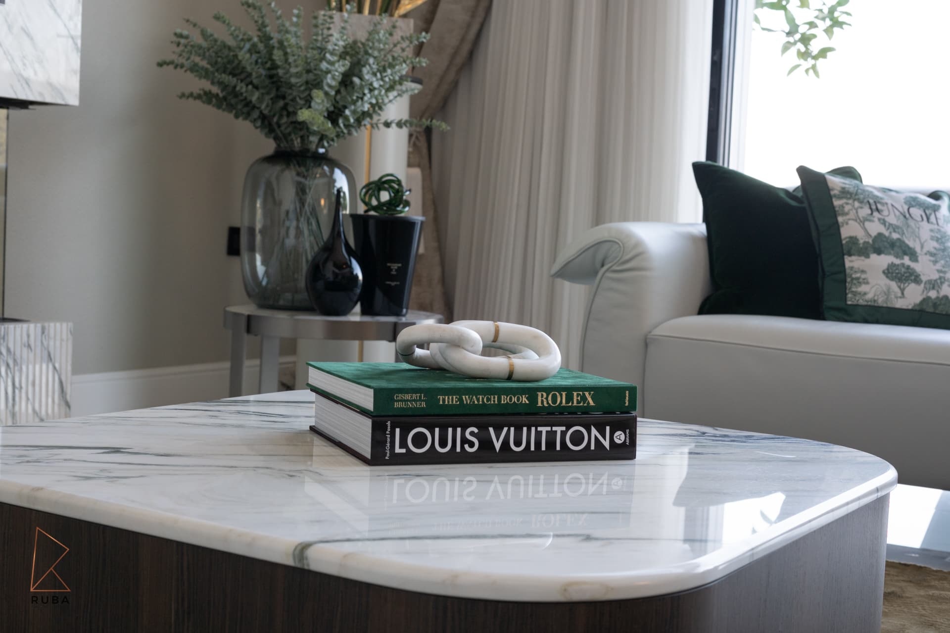 Books and a white marble chain sculpture on a veined marble coffee table in the living room of Bird of Paradise Flower