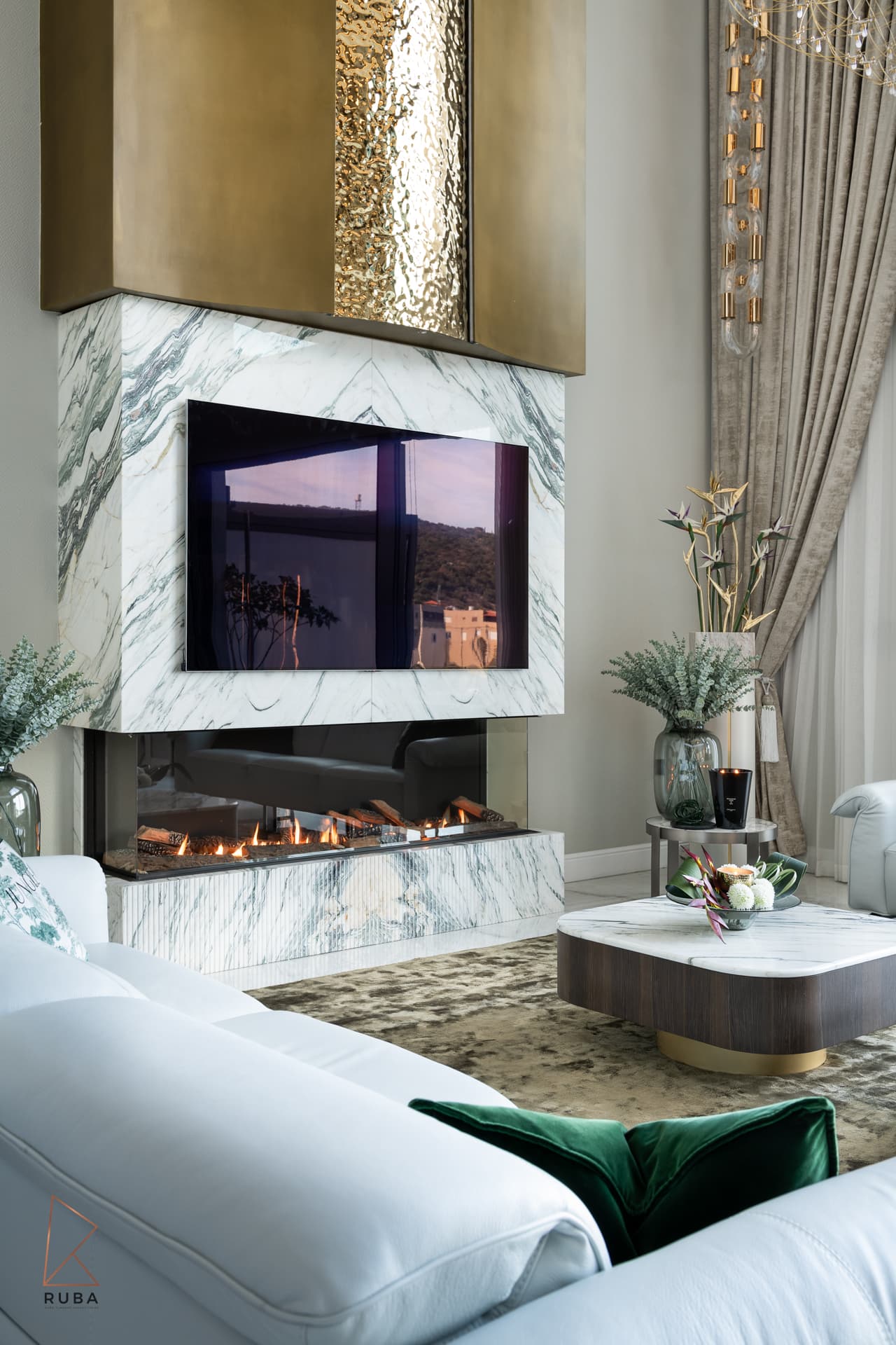 Corner gas fireplace with a fluted marble base and hammered brass hood above the white sofa in the living room of Bird of Paradise Flower