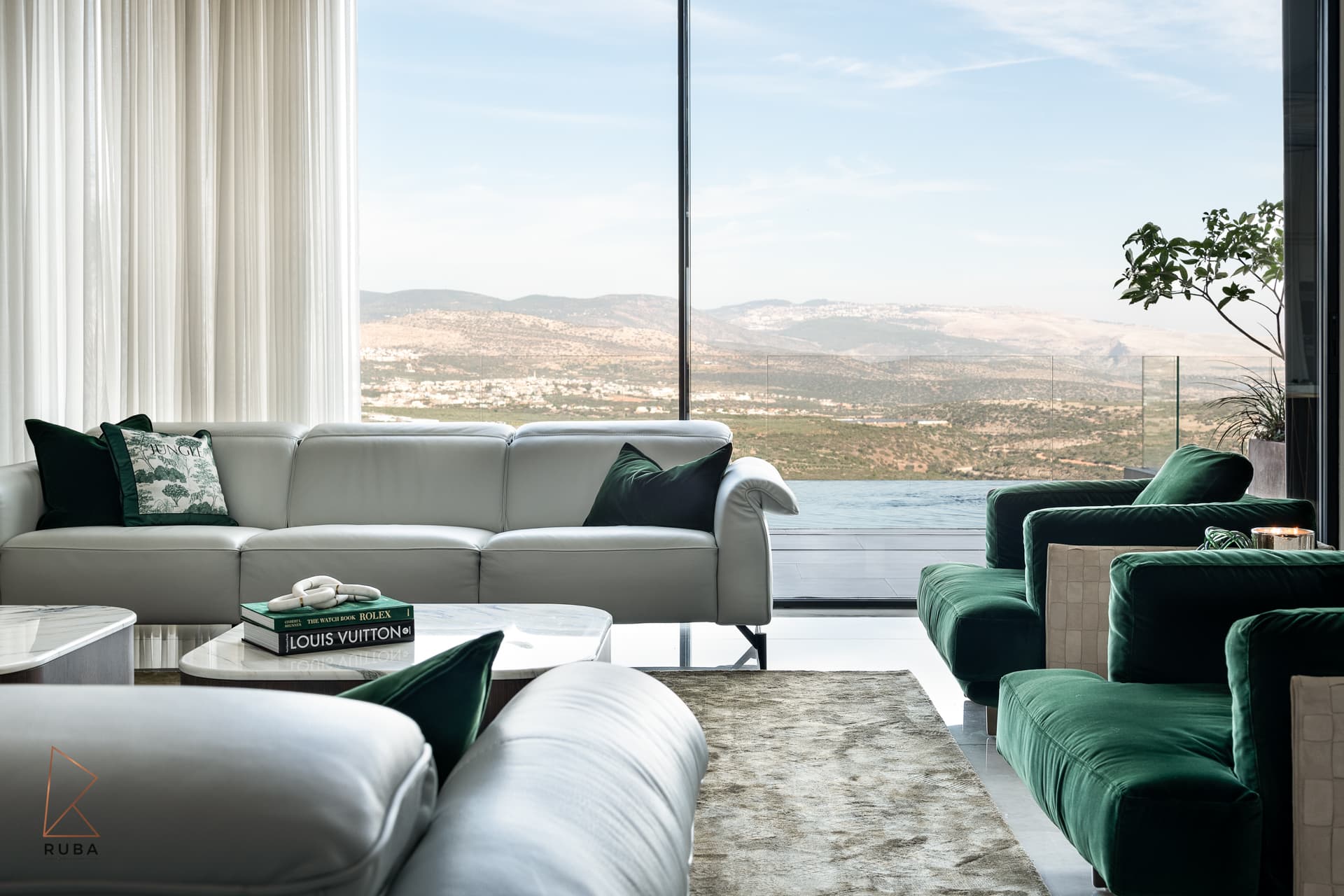 White leather sofa and green velvet armchairs before a full-height window onto the valley in the living room of Bird of Paradise Flower
