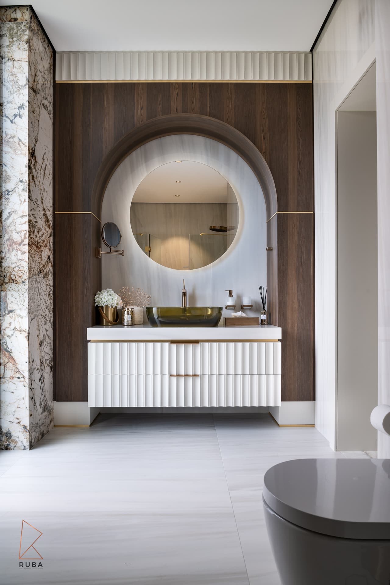 Floating fluted white vanity under an arched niche with a round backlit mirror in the master bathroom of Bird of Paradise Flower