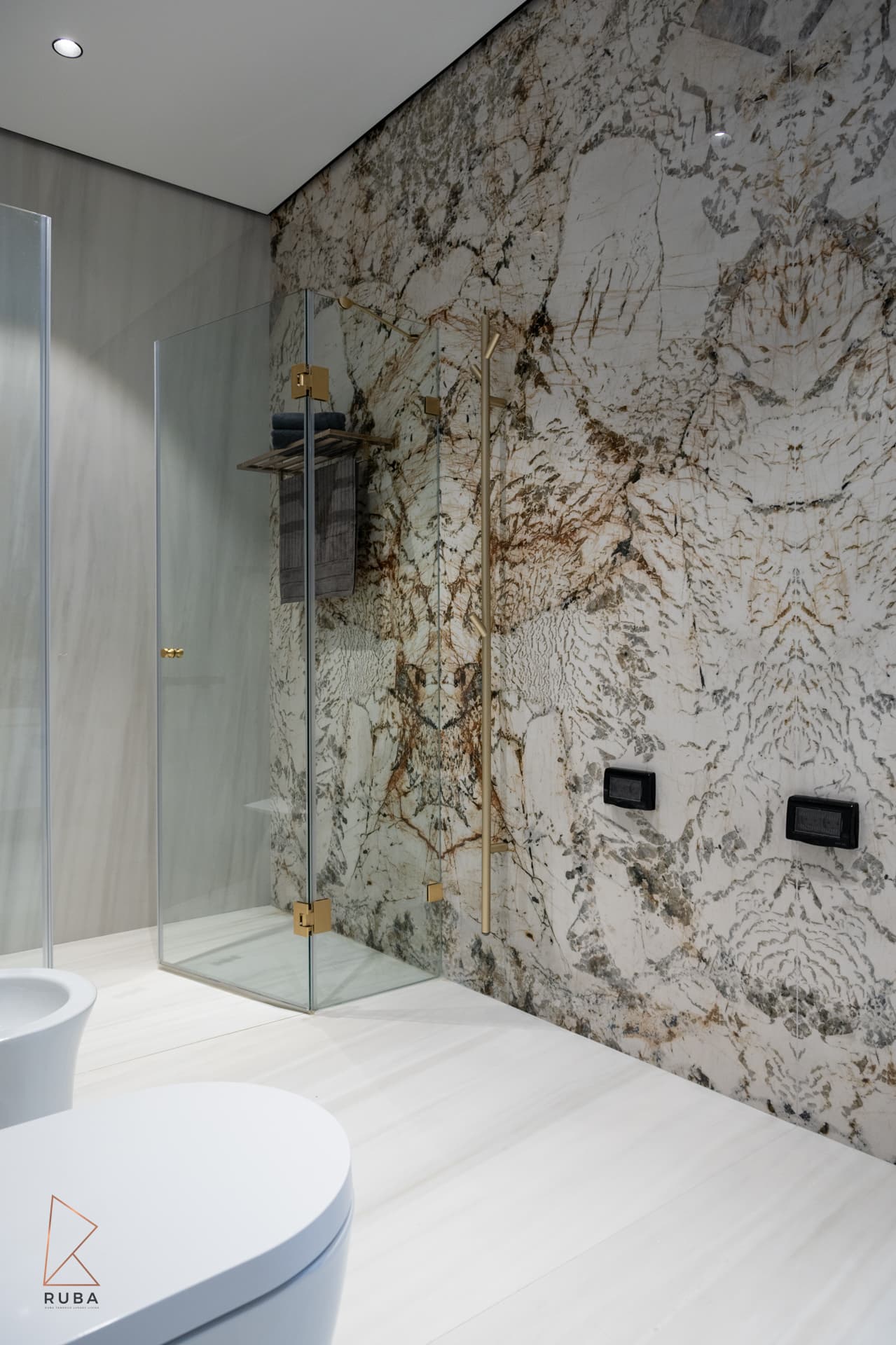 Walk-in glass shower against a brown-veined stone feature wall with brass fittings in the master bathroom of Bird of Paradise Flower