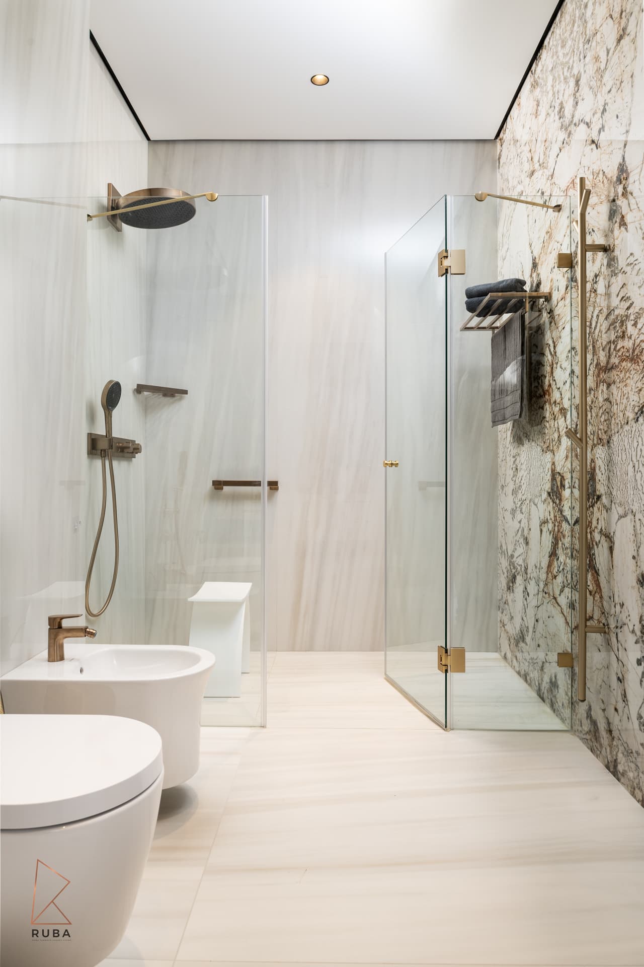 Two glass showers with a bronze rain head and a bidet against pale striated stone in the master bathroom of Bird of Paradise Flower