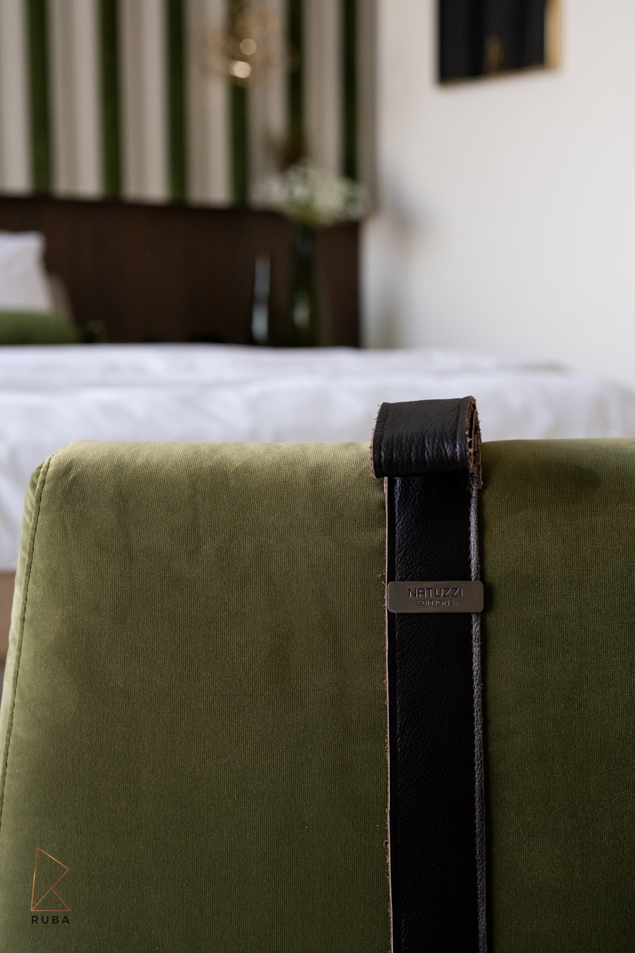 Sage velvet chair back with a black leather strap, the bed softly blurred behind, in the master bedroom of Bird of Paradise Flower