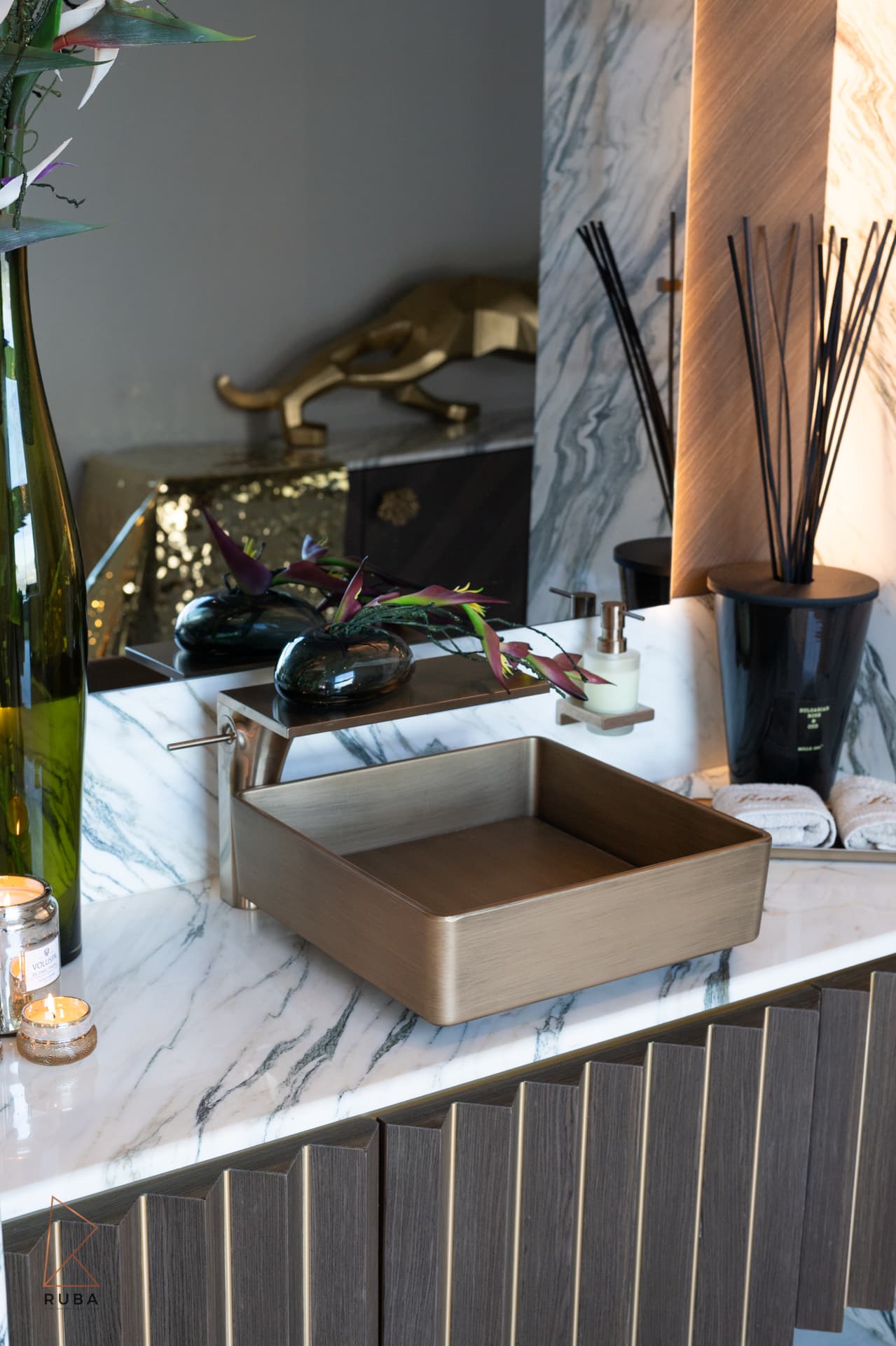 Square brushed brass basin on a veined marble counter over a fluted wood vanity in the powder room of Bird of Paradise Flower