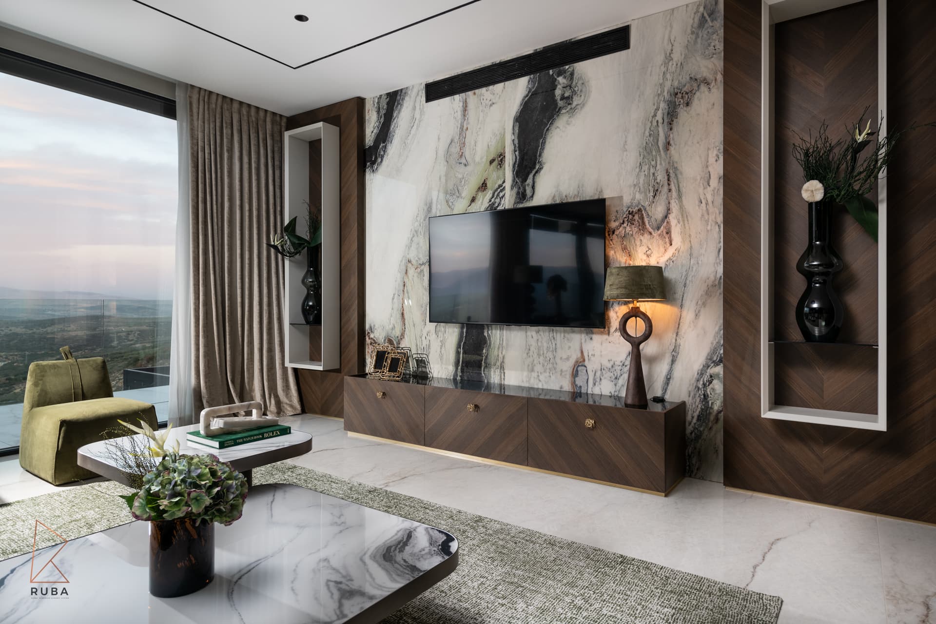Bookmatched marble media wall flanked by wood niches, with a chevron console and sage armchair, in the salon of Bird of Paradise Flower