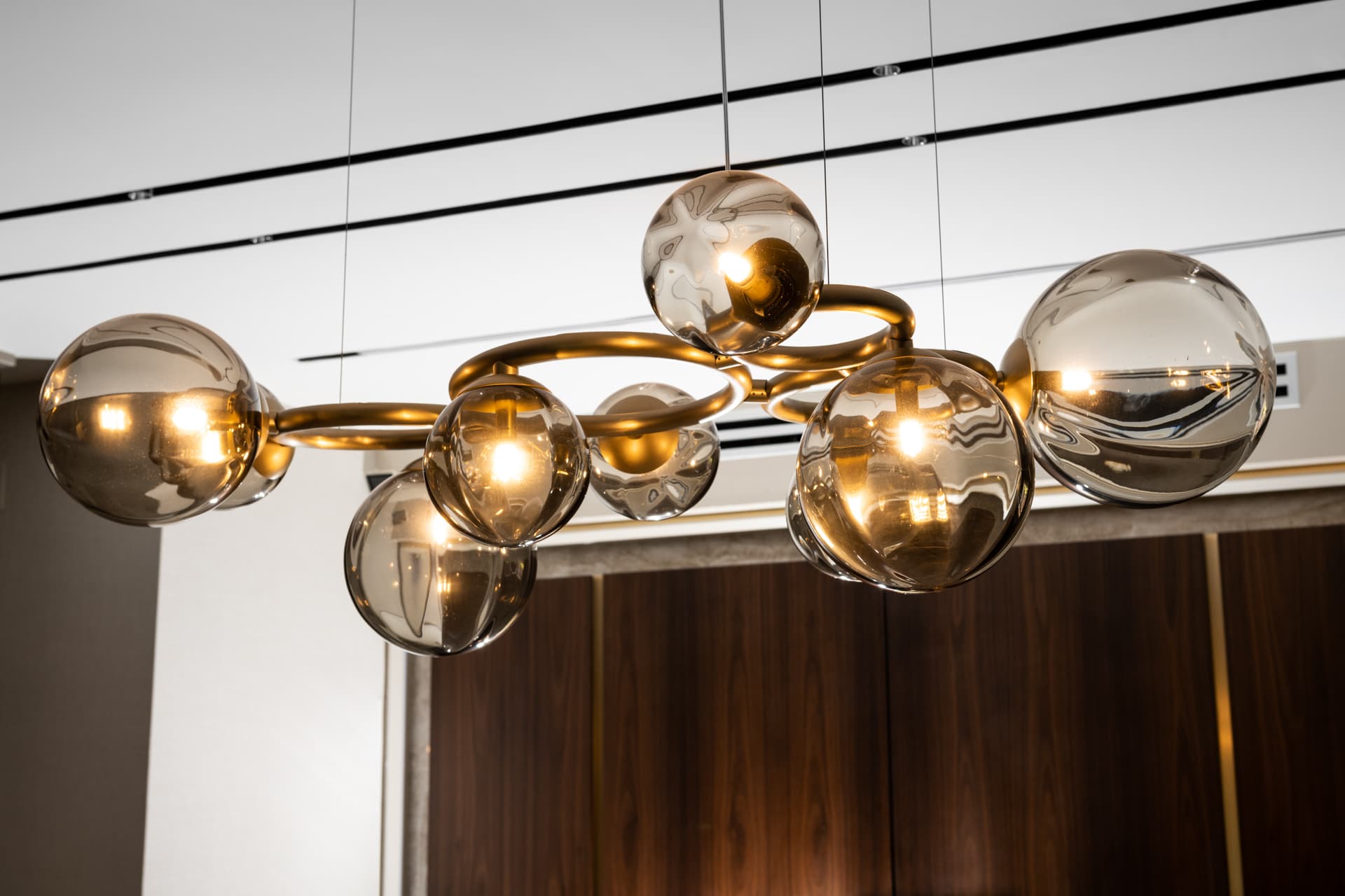 Smoked-glass globe chandelier on looping brass arms hanging before walnut paneling in Born Together