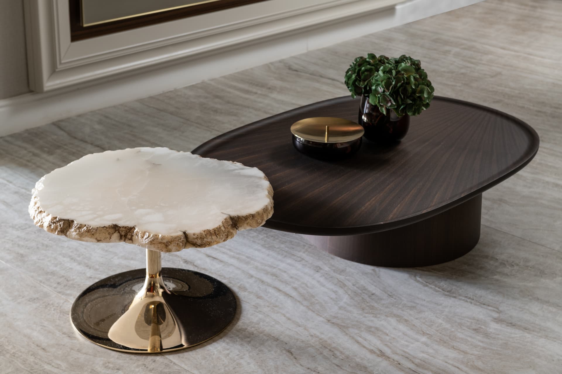 Raw-edge white stone side table with a brass base beside a dark oval walnut coffee table in Born Together