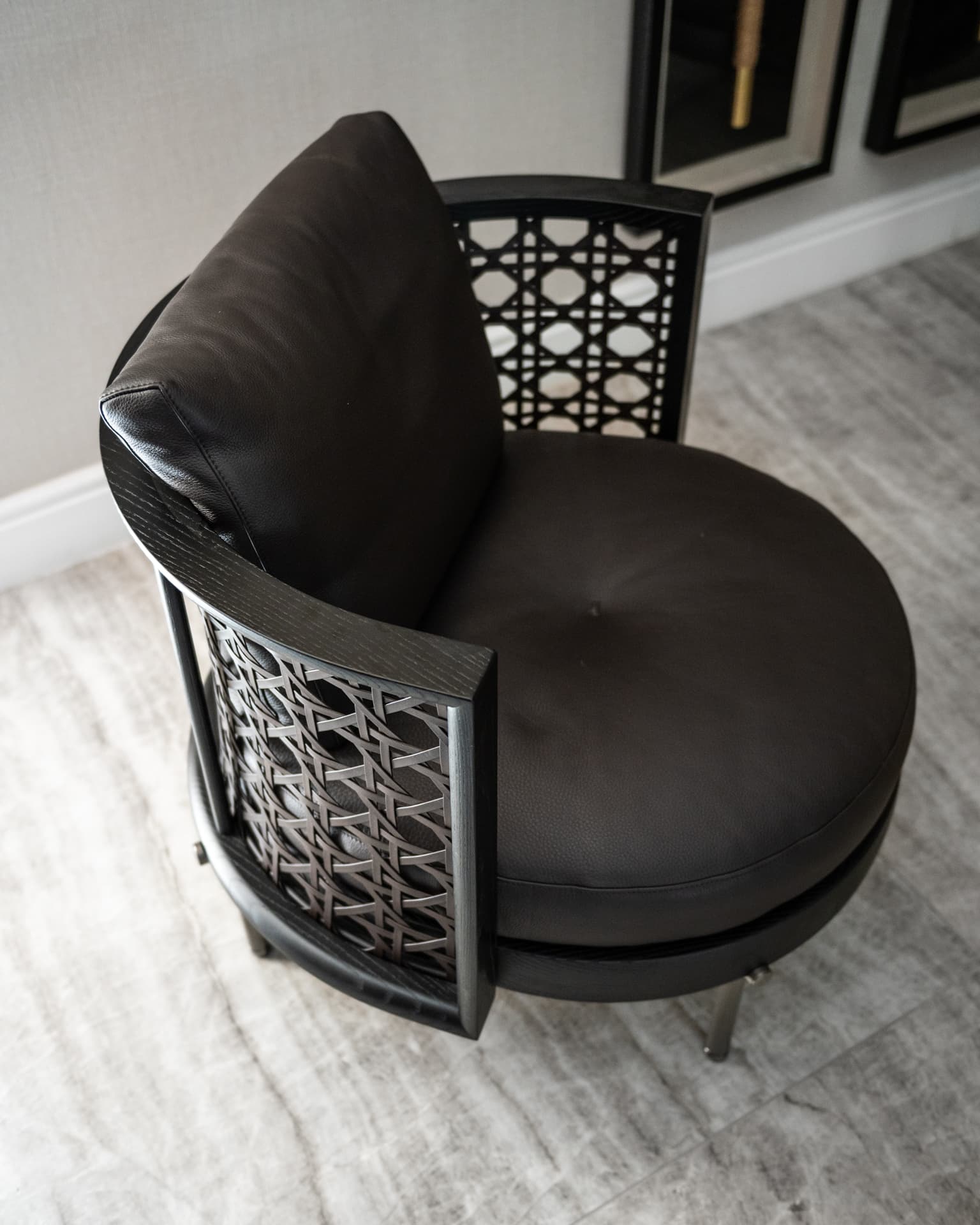 Overhead view of a black leather armchair with a curved lattice back on a veined stone floor in Born Together