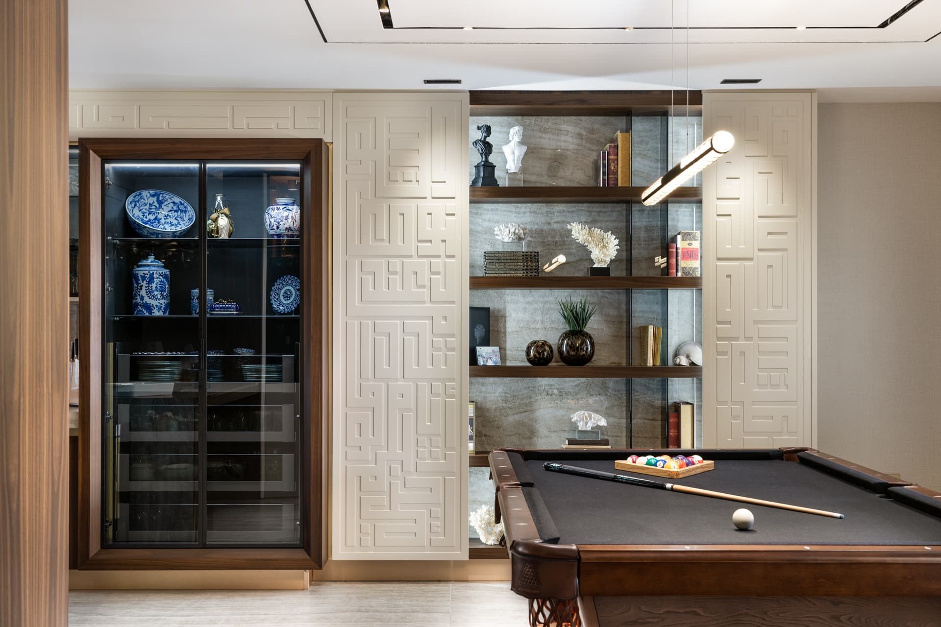 Game room with a billiard table, glass-front china cabinet and shelving set between geometric relief panels in Born Together