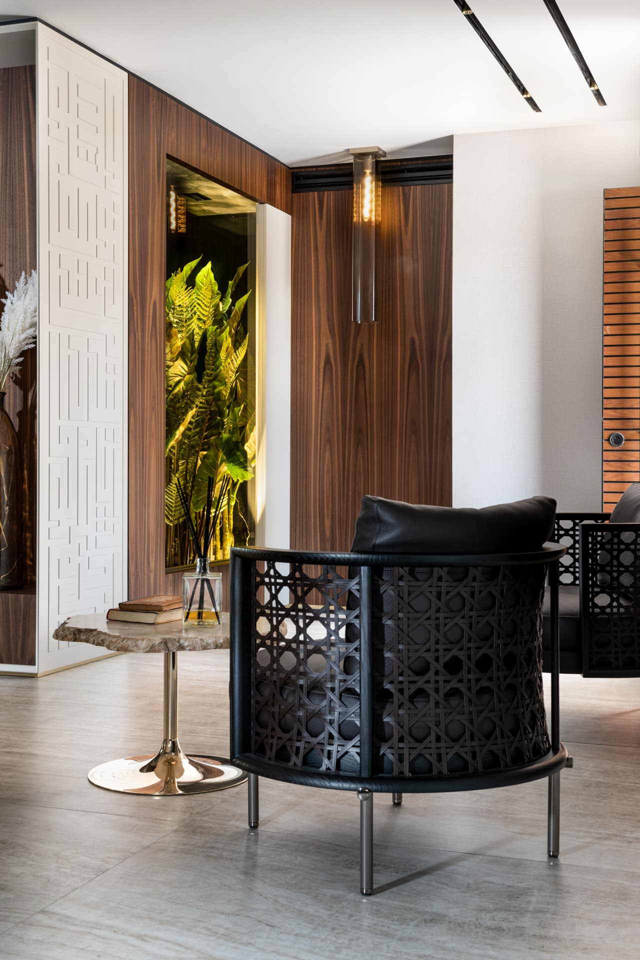 Hallway with a black lattice armchair, stone side table and lit planter niche against walnut paneling in Born Together