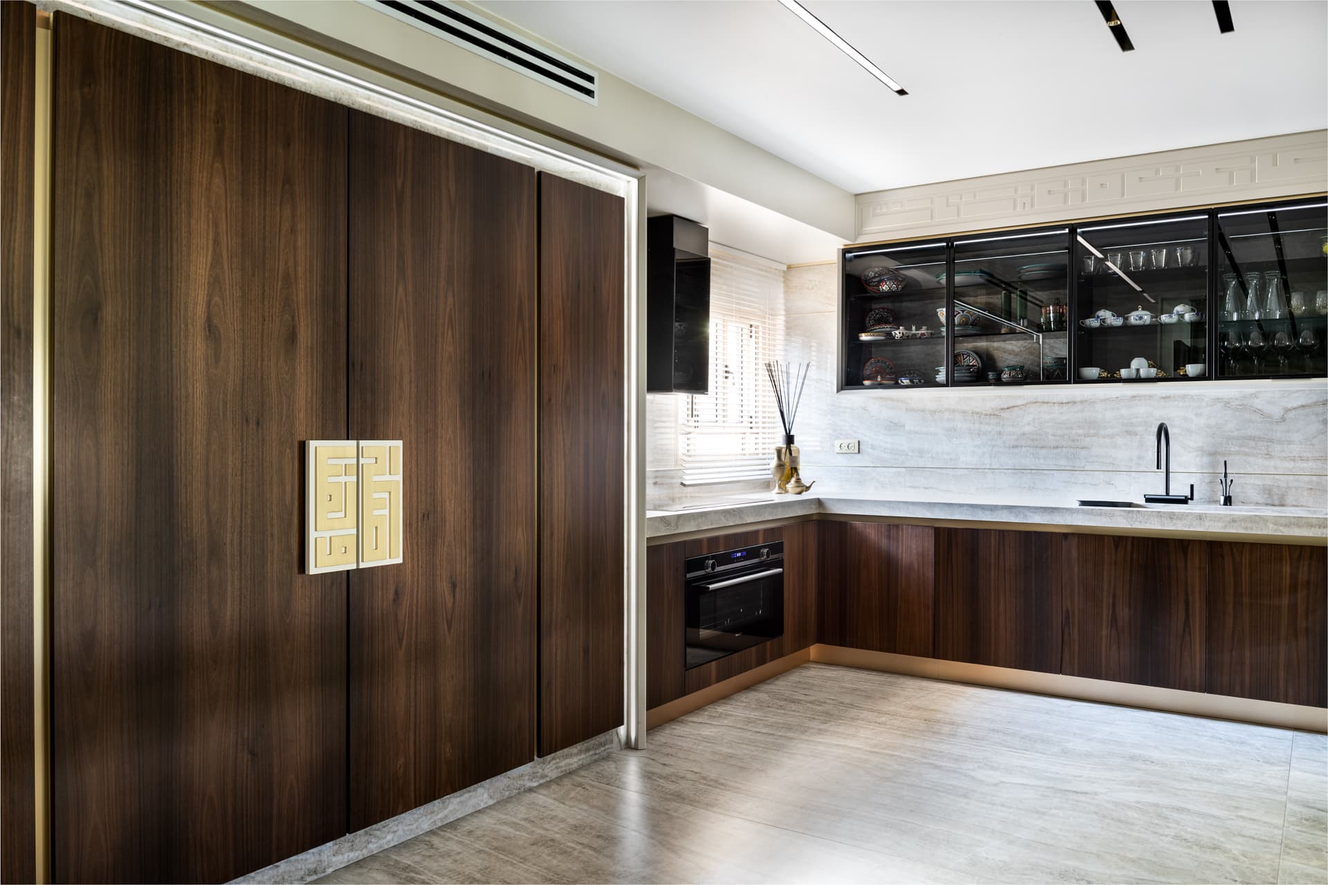 Kitchen with a wall of walnut doors, a brass geometric door pull and black glass-front upper cabinets in Born Together