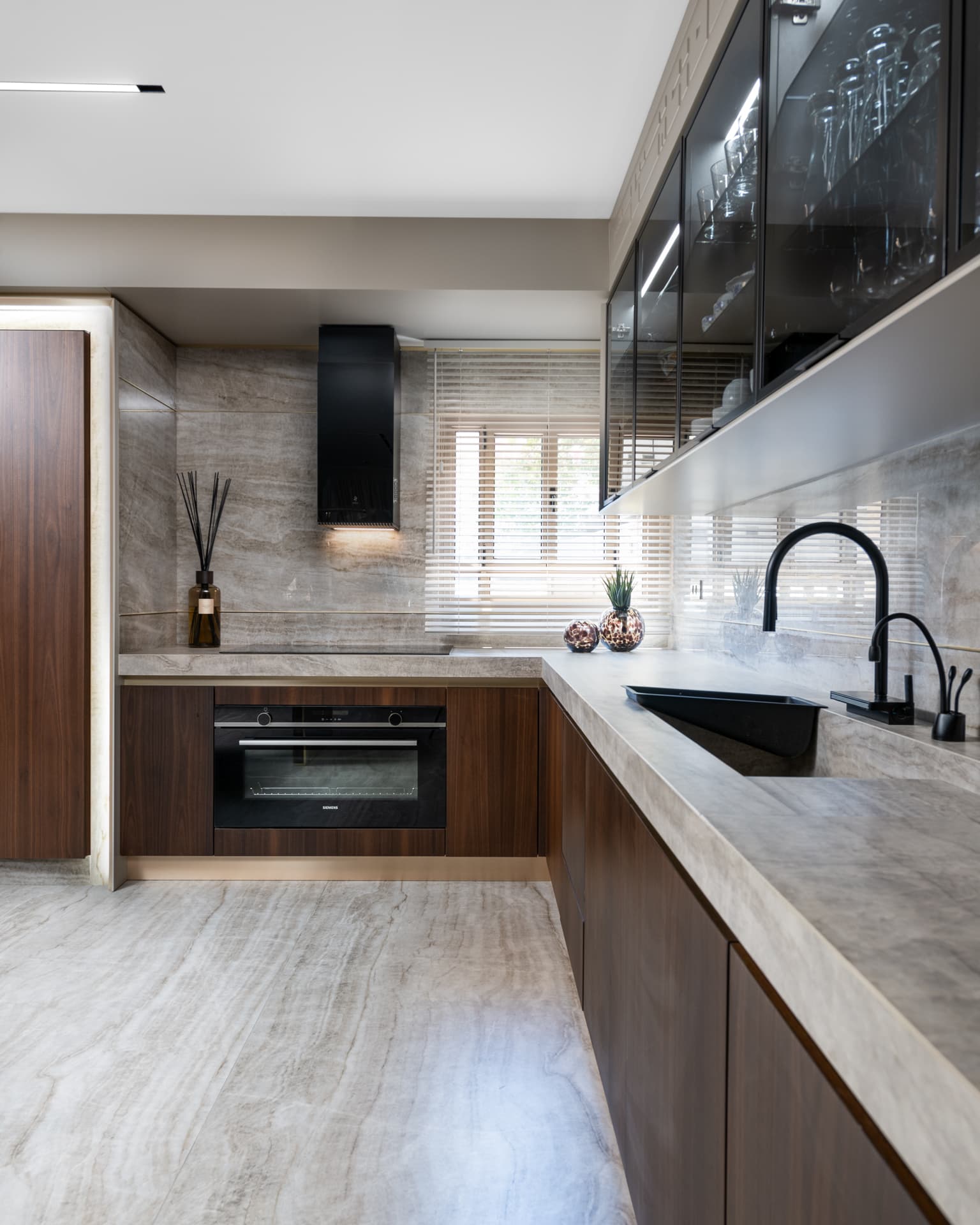 Kitchen with walnut base cabinets, a veined stone counter and backsplash, and a black faucet and sink in Born Together