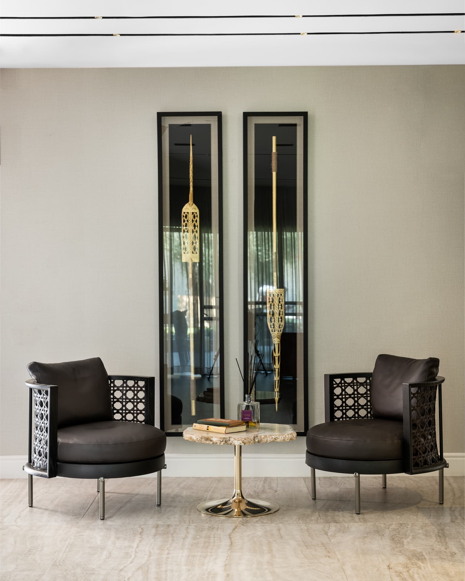 Two black leather lattice-sided armchairs and a stone side table between tall framed gilt ornaments in the living room of Born Together