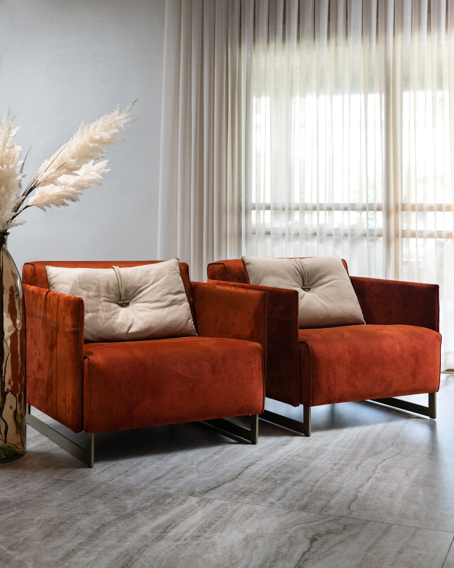Pair of rust velvet armchairs with cream cushions before sheer curtains in the living room of Born Together