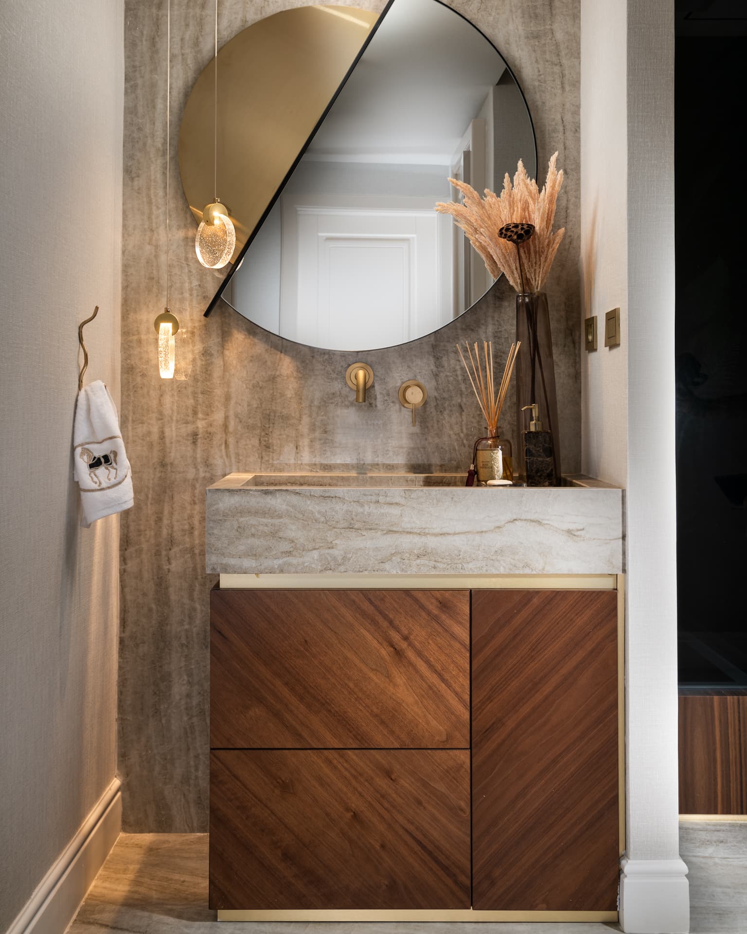 Powder room with a veined stone basin on a walnut vanity, a split round mirror and brass wall taps in Born Together