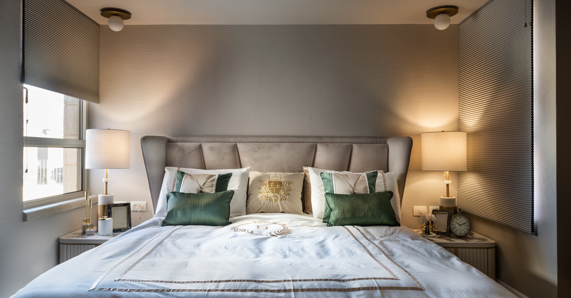 Bedroom with a winged, channel-tufted headboard, green velvet cushions and matching lamps on fluted nightstands in Cognac